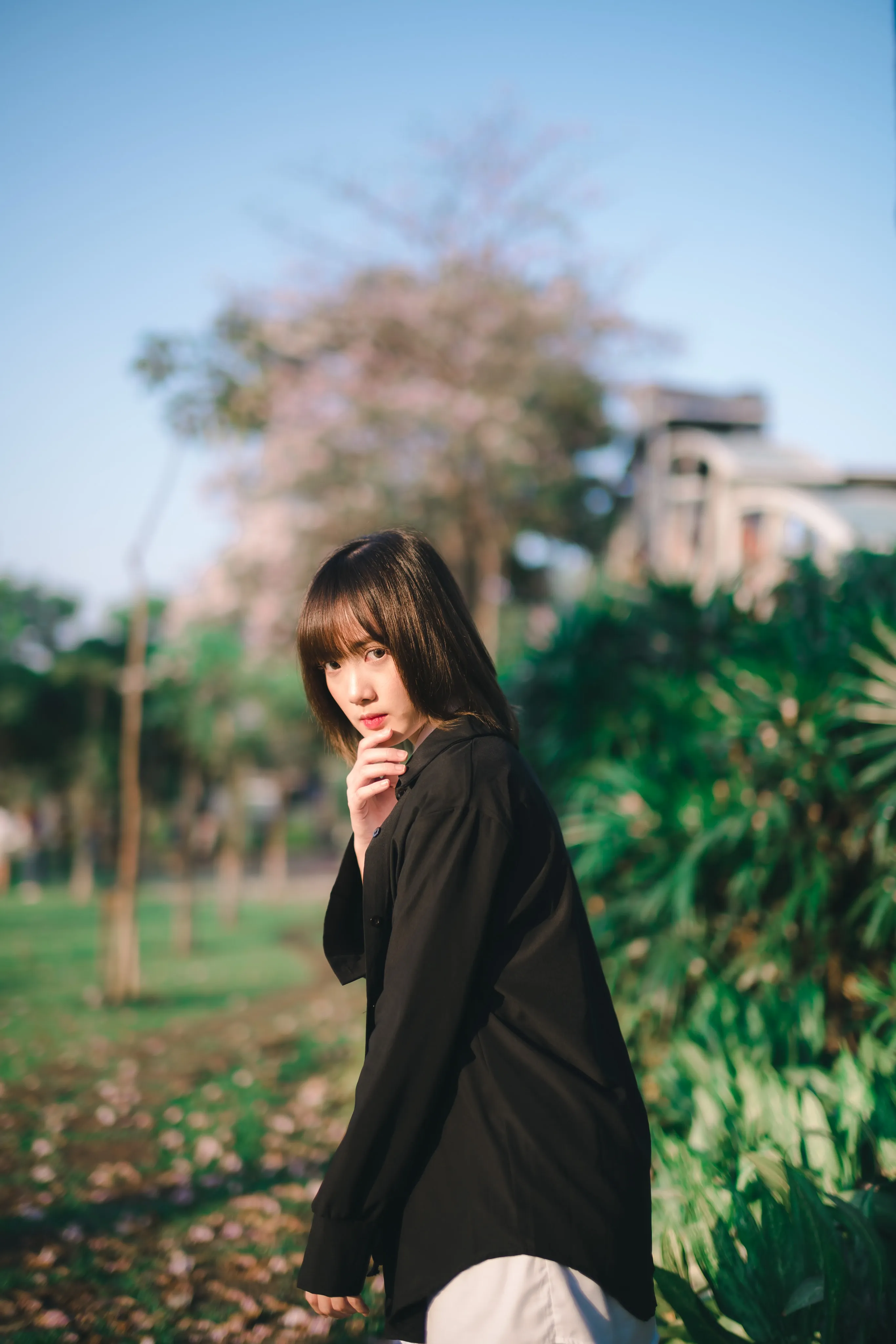 A young woman in a black shirt looking back at the camera in a park with pink blossom trees