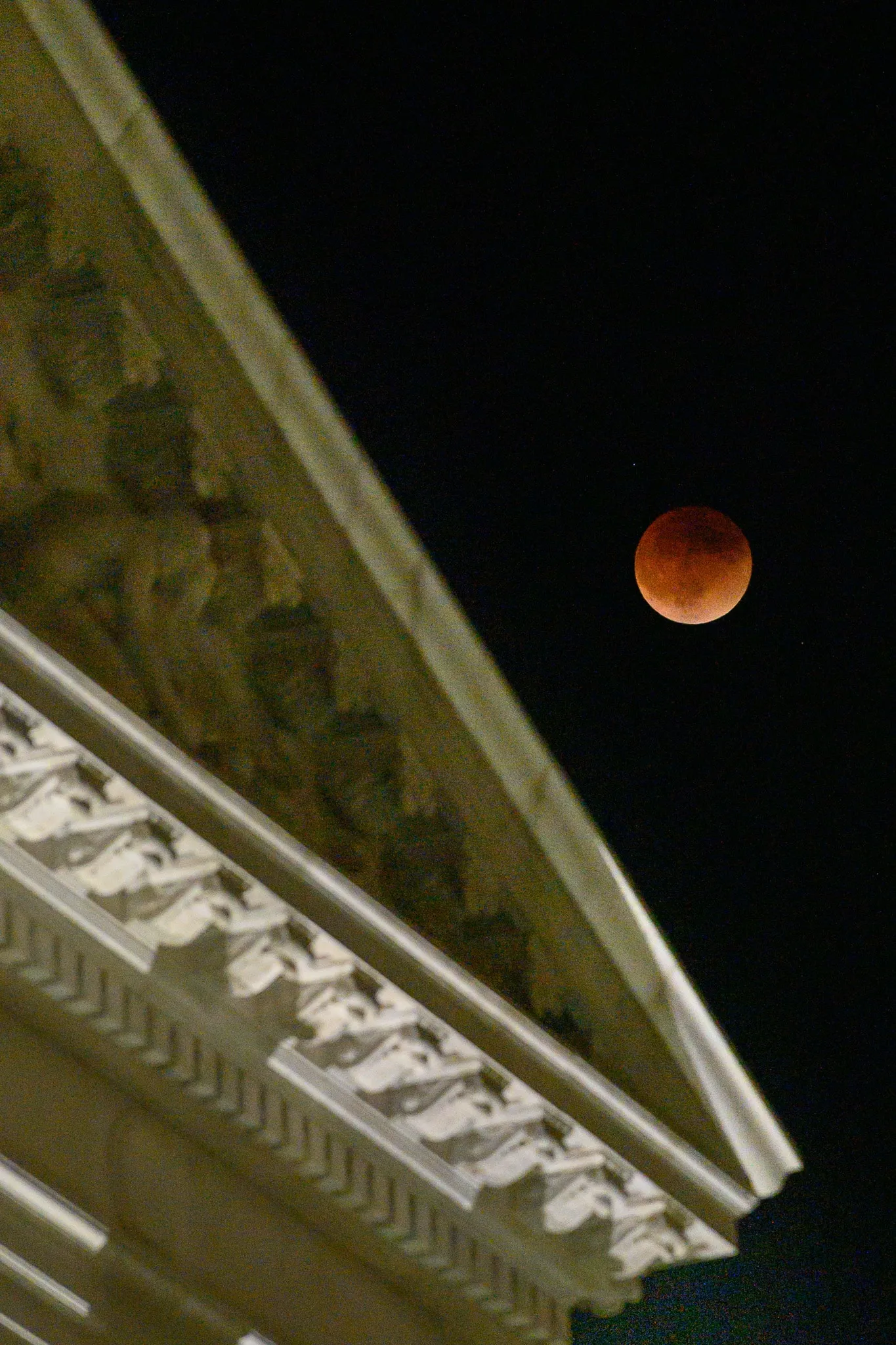 Orange-red lunar eclipse above the illuminated edge of a building
