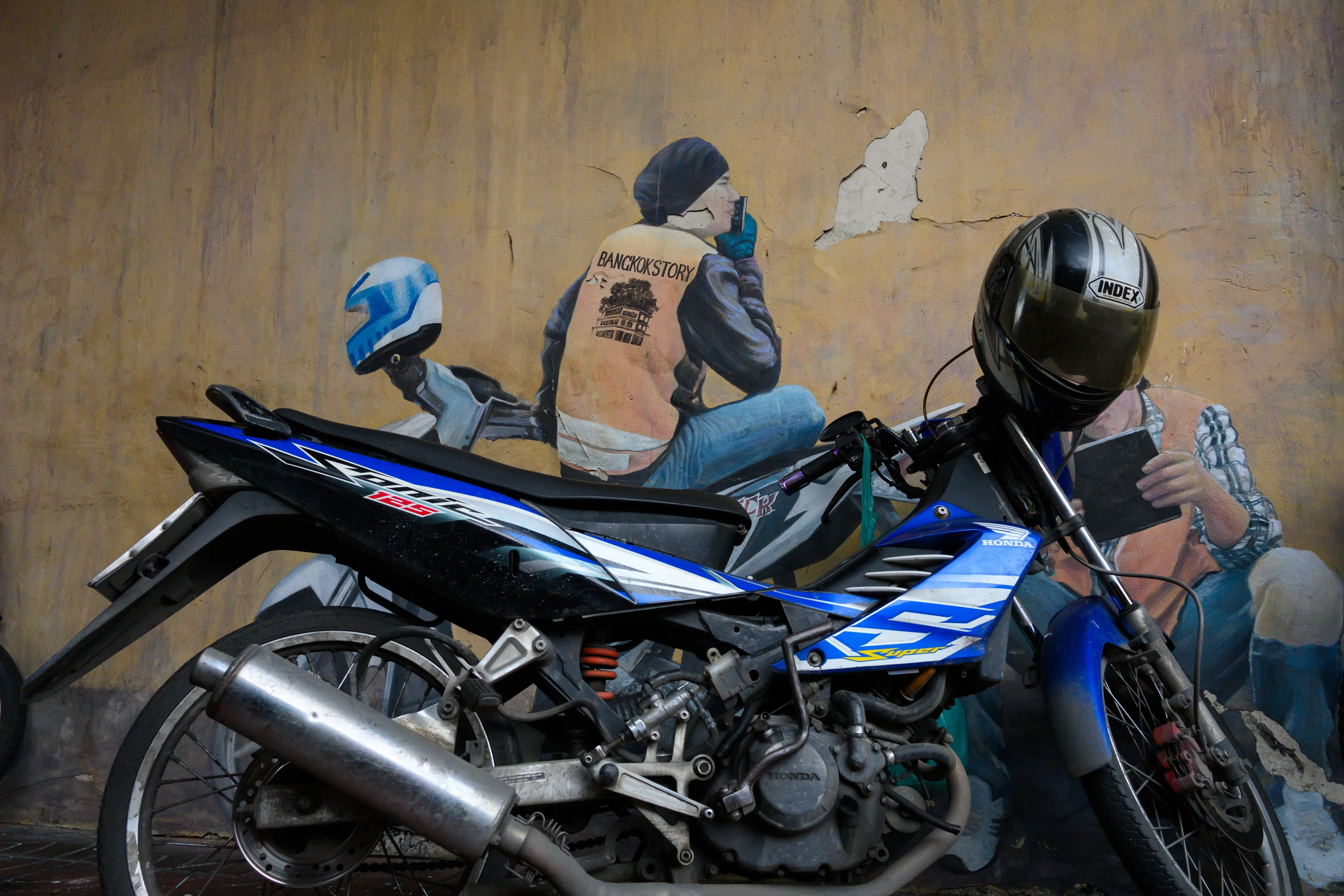 Parked motorcycles aligned with painted riders on a worn wall mural