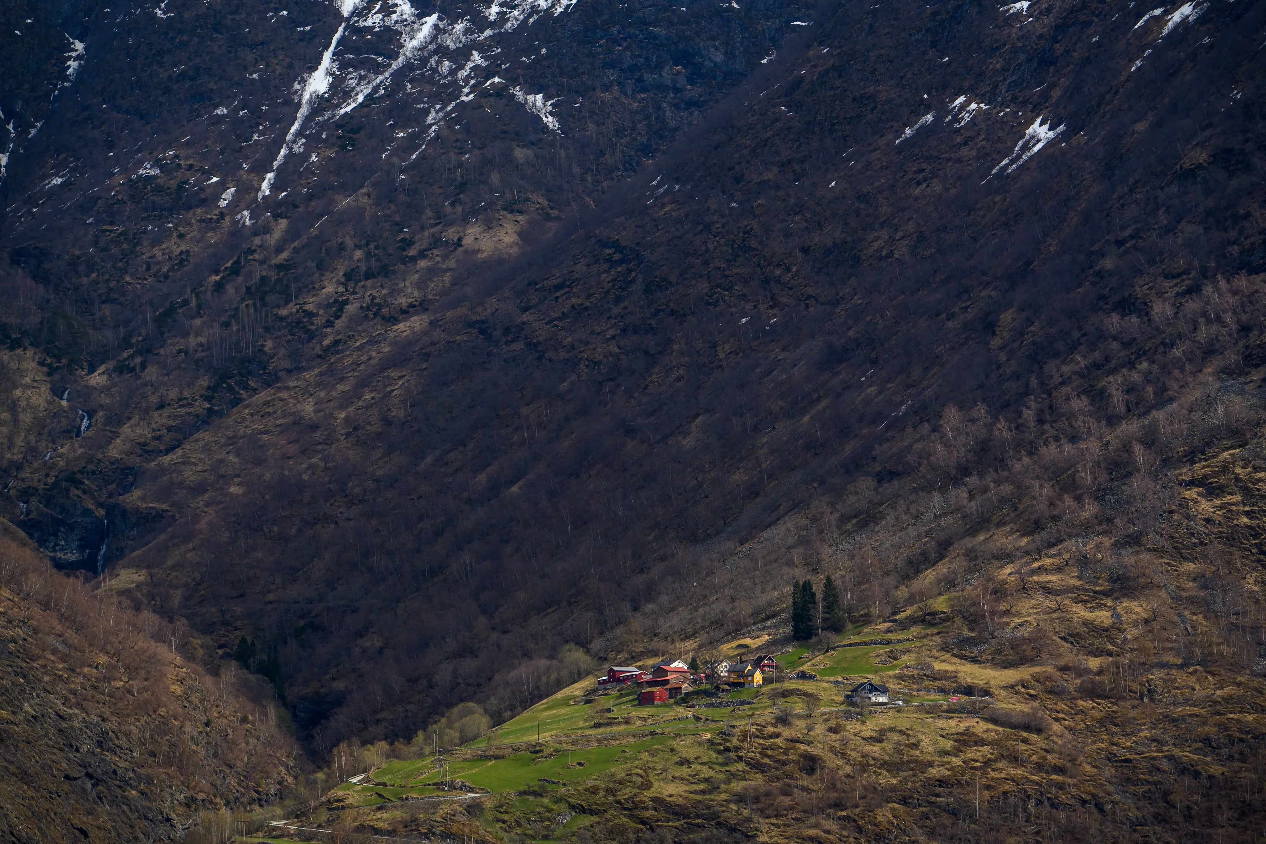 A small farmstead perched on a steep, snow-streaked mountainside