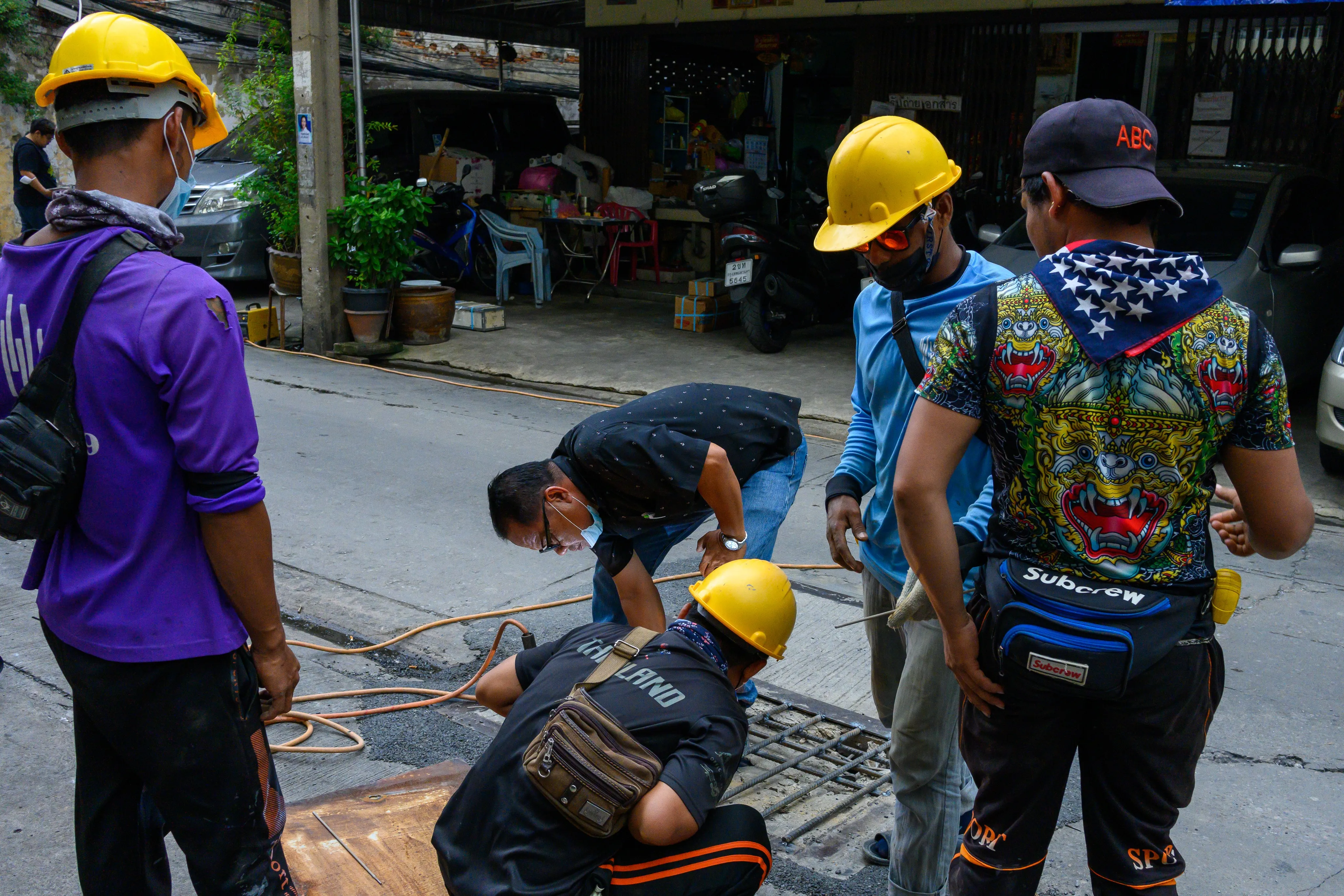 Road workers in yellow hard hats gathered around a work site