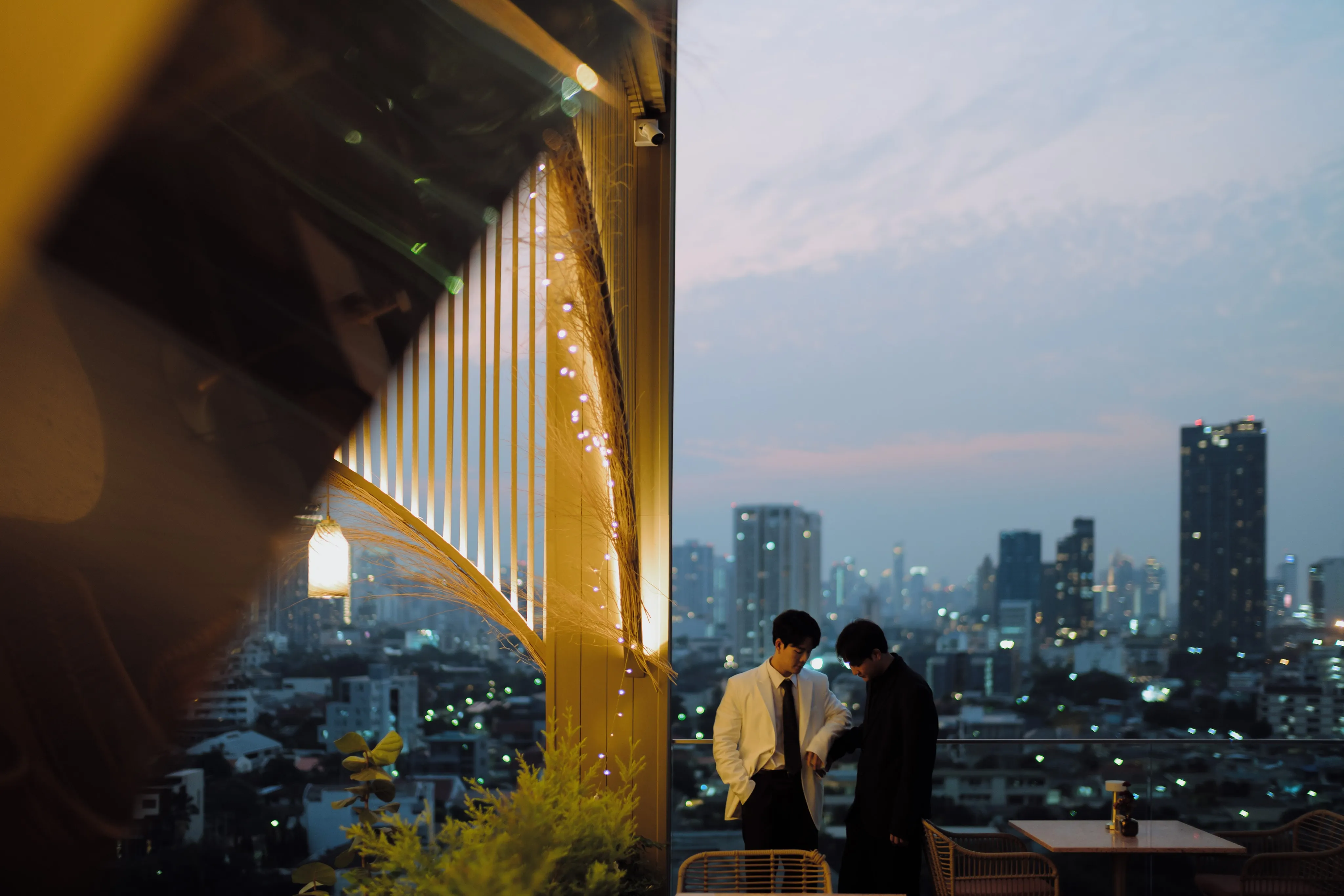 Two men in suits standing on a rooftop terrace overlooking the city at dusk