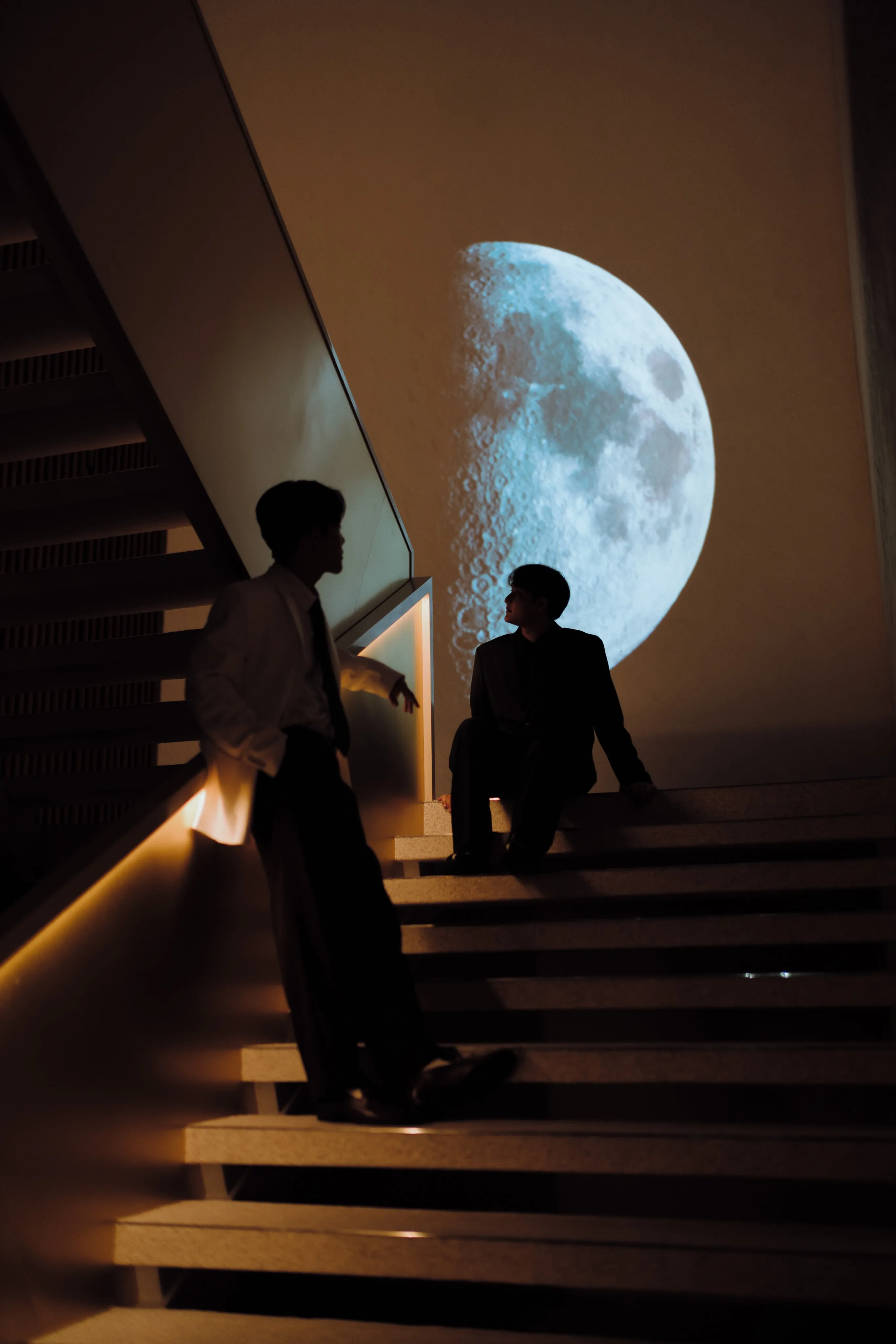 Two men silhouetted on a staircase in front of a large illuminated moon