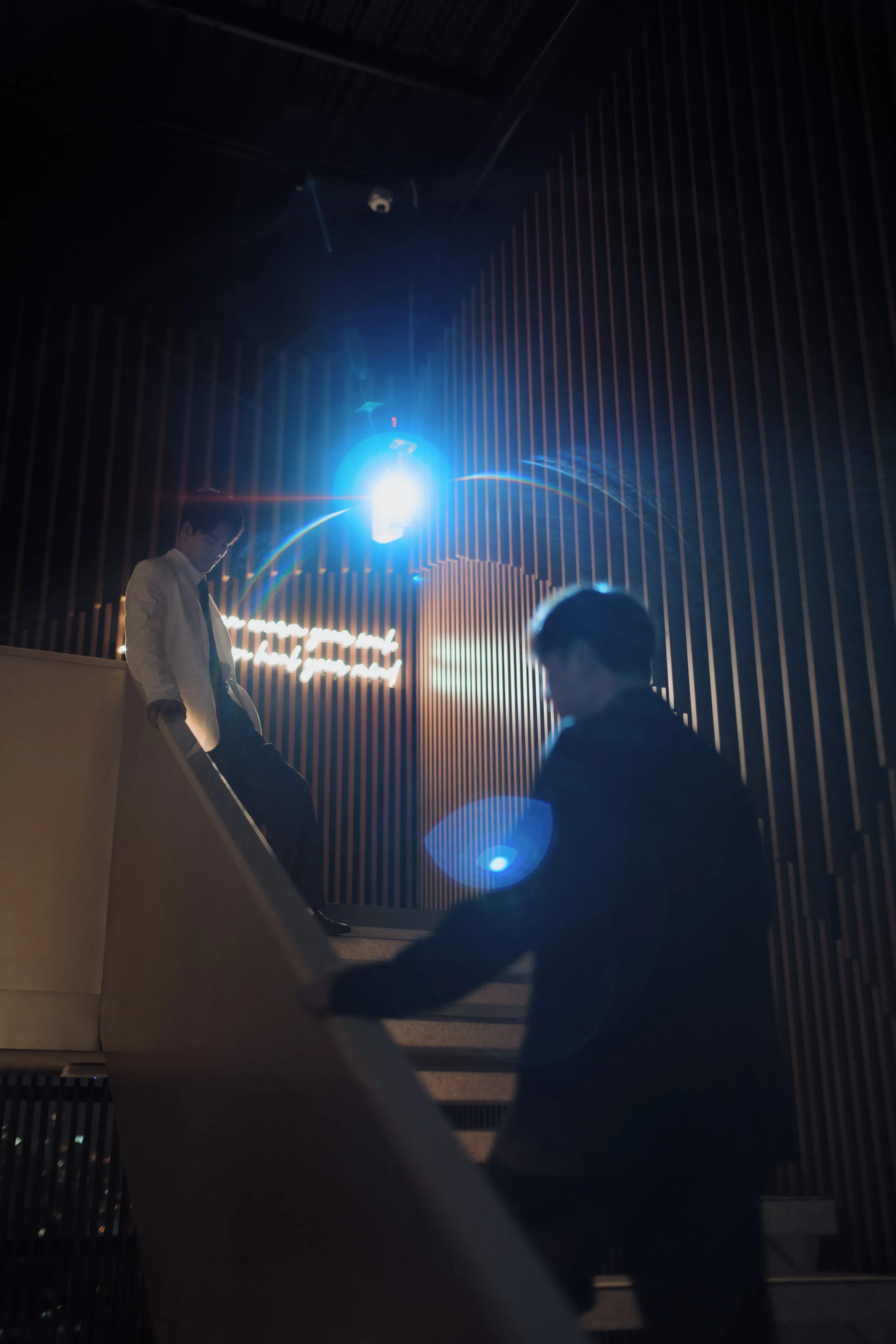 Two men on a dark staircase with a blue spotlight flaring behind them