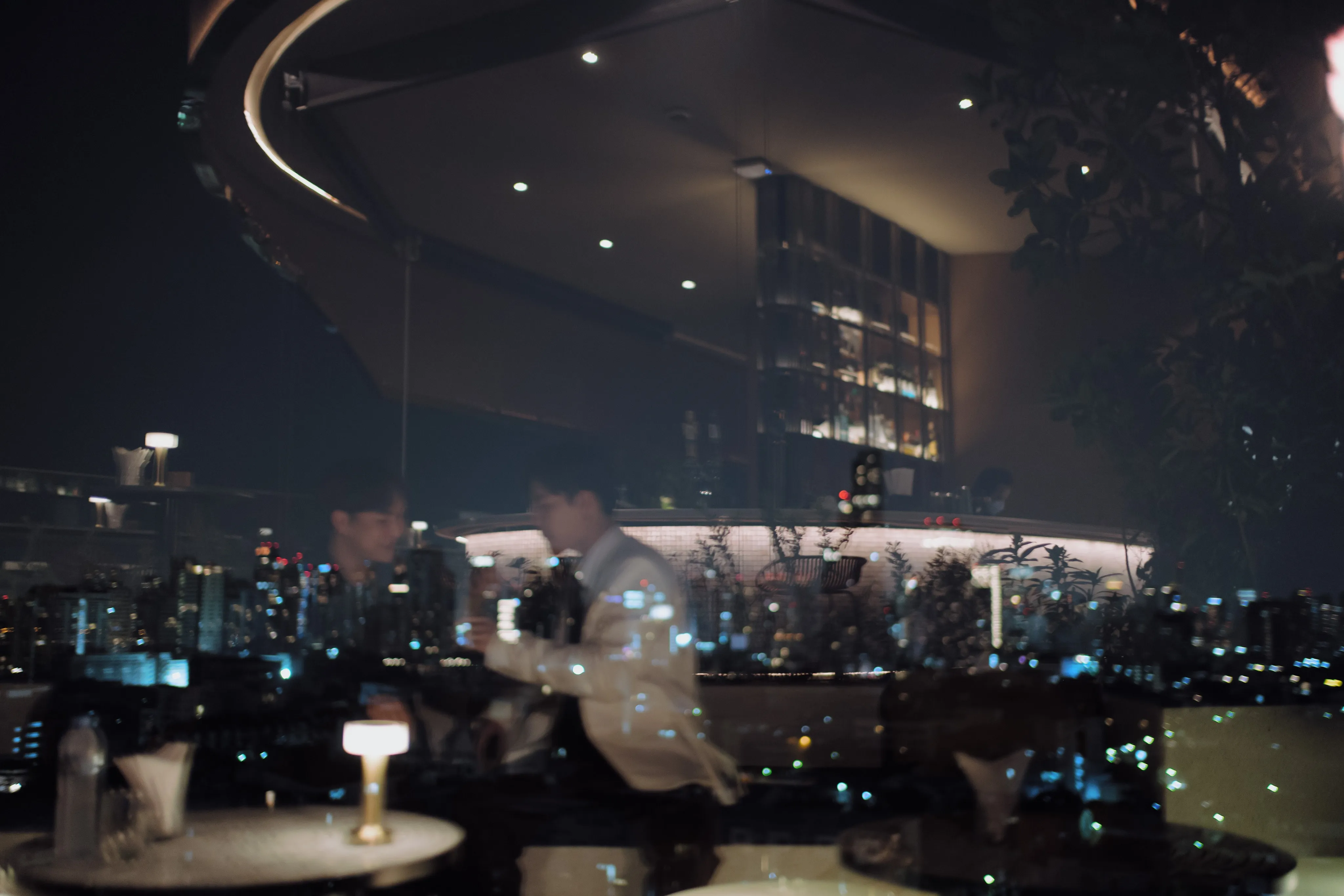 Two men at a rooftop bar at night above the lights of the city