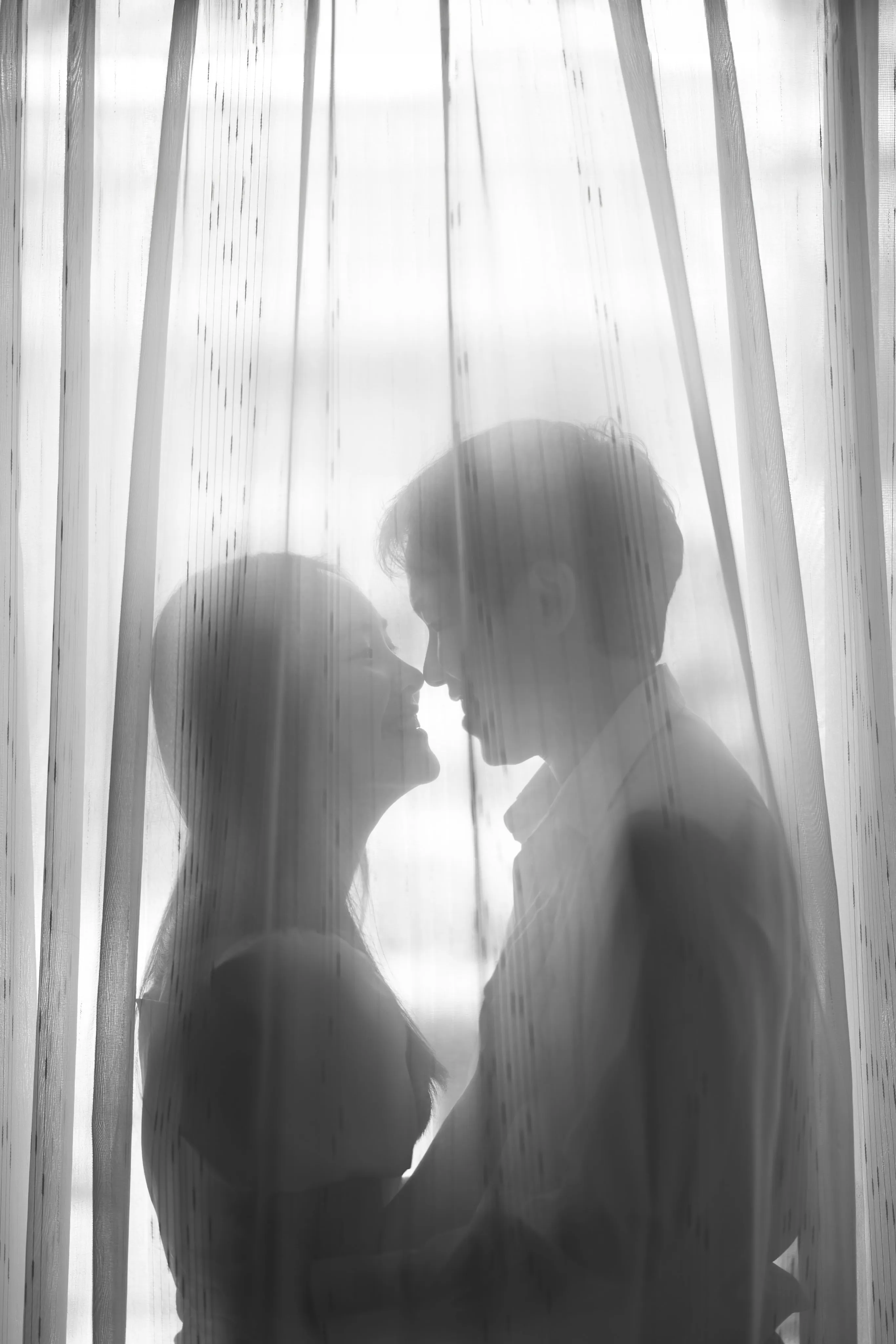 A couple's silhouette kissing behind sheer curtains