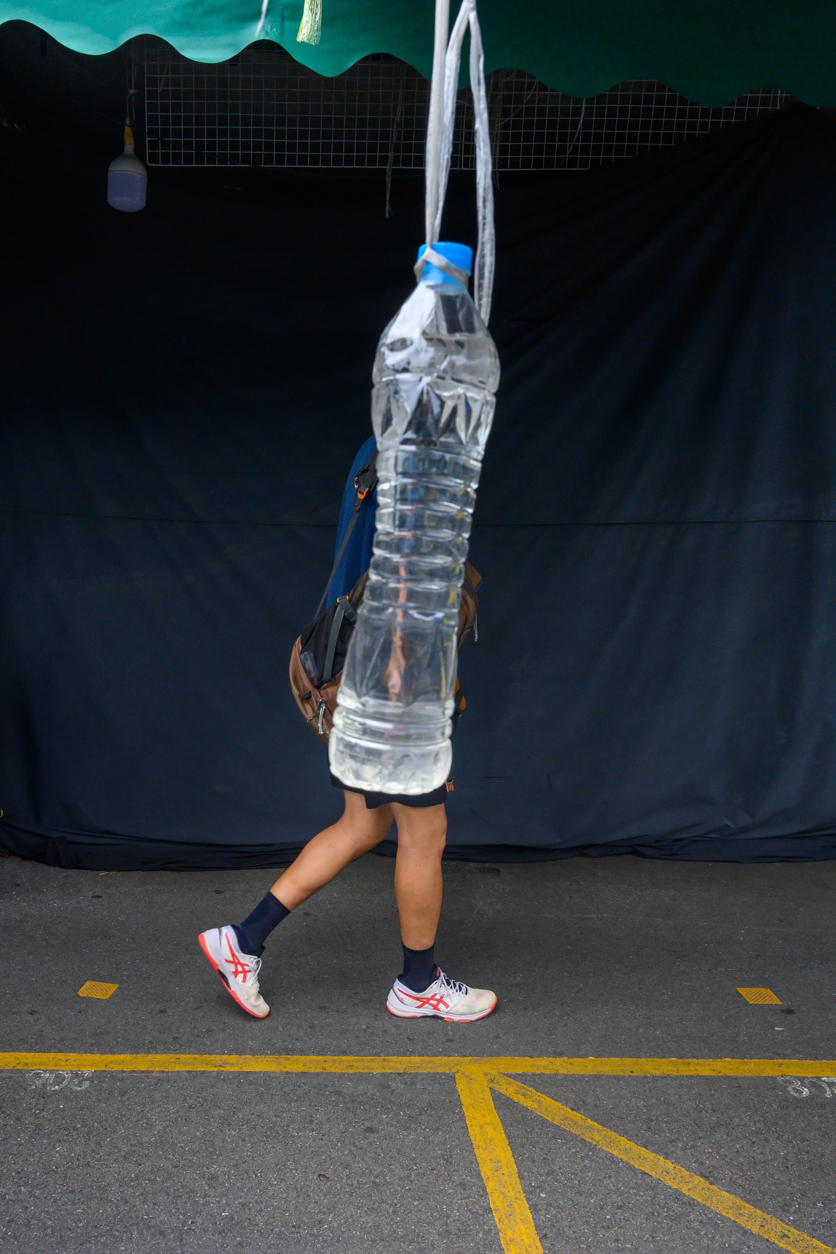 Pedestrian carrying a large hanging bundle of plastic bottles against a dark backdrop