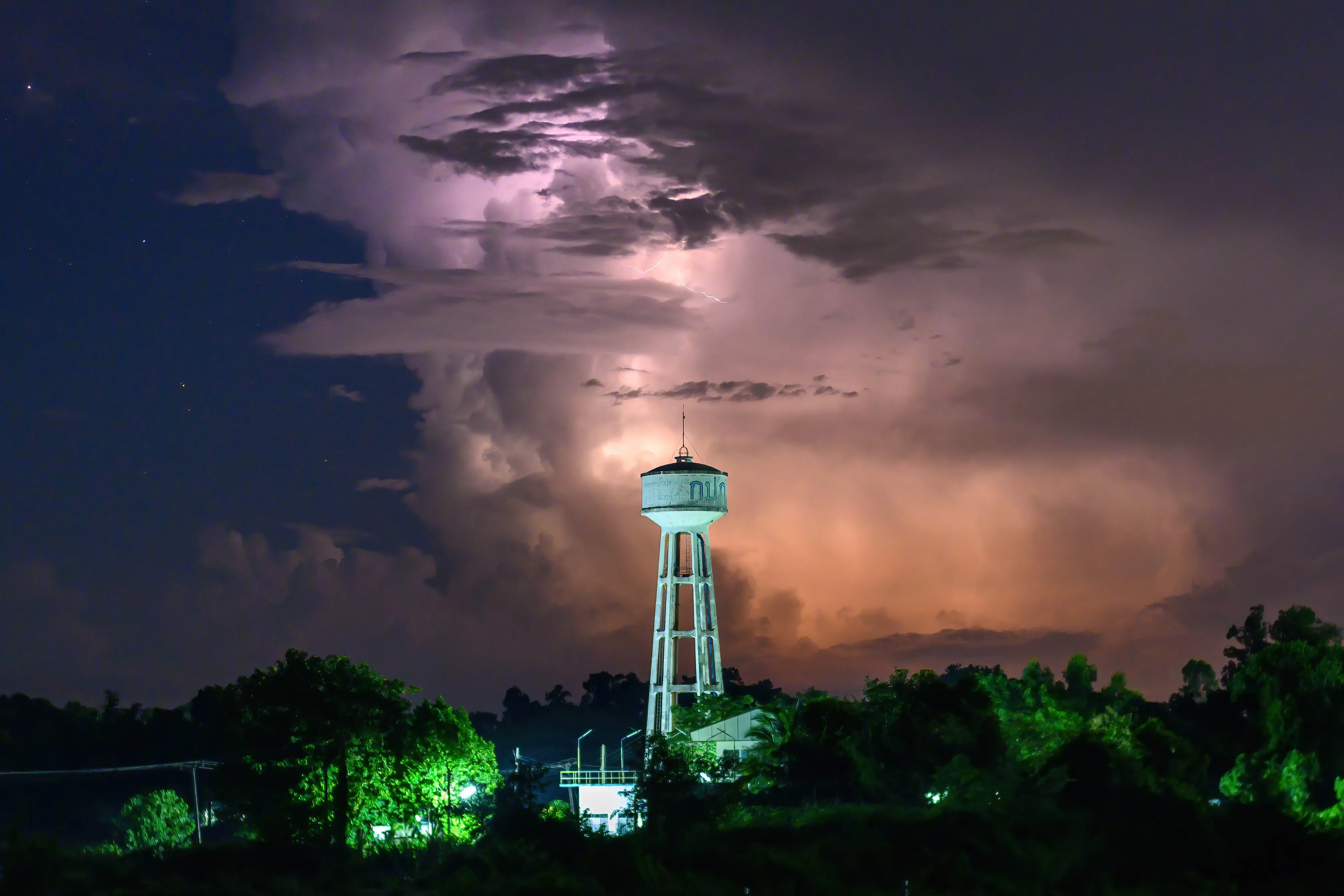 Lightning illuminating storm clouds behind a lit water tower