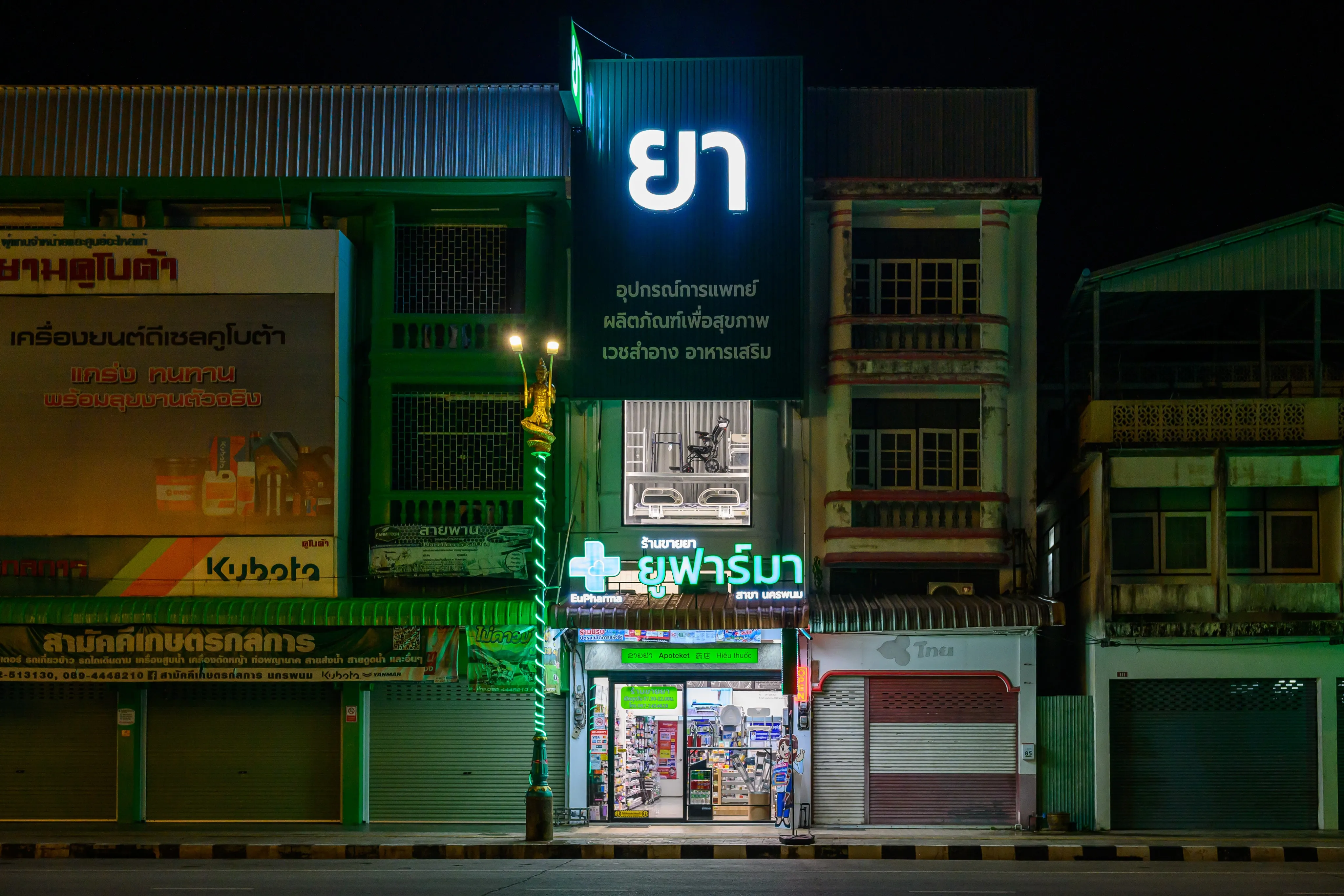 A pharmacy storefront illuminated by green and blue signs at night