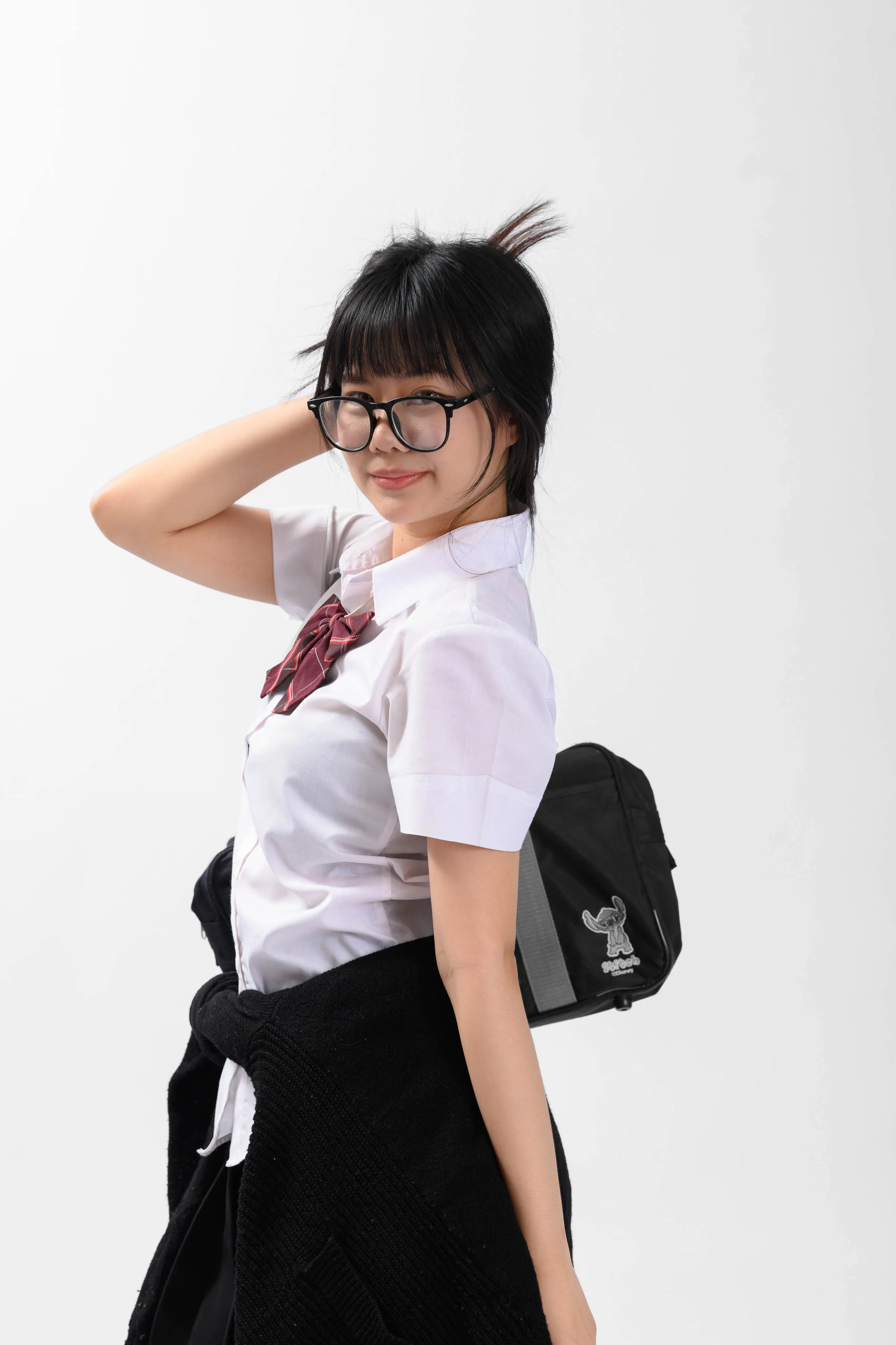 A young woman in glasses and a white school shirt with a bow posing with a hand behind her head