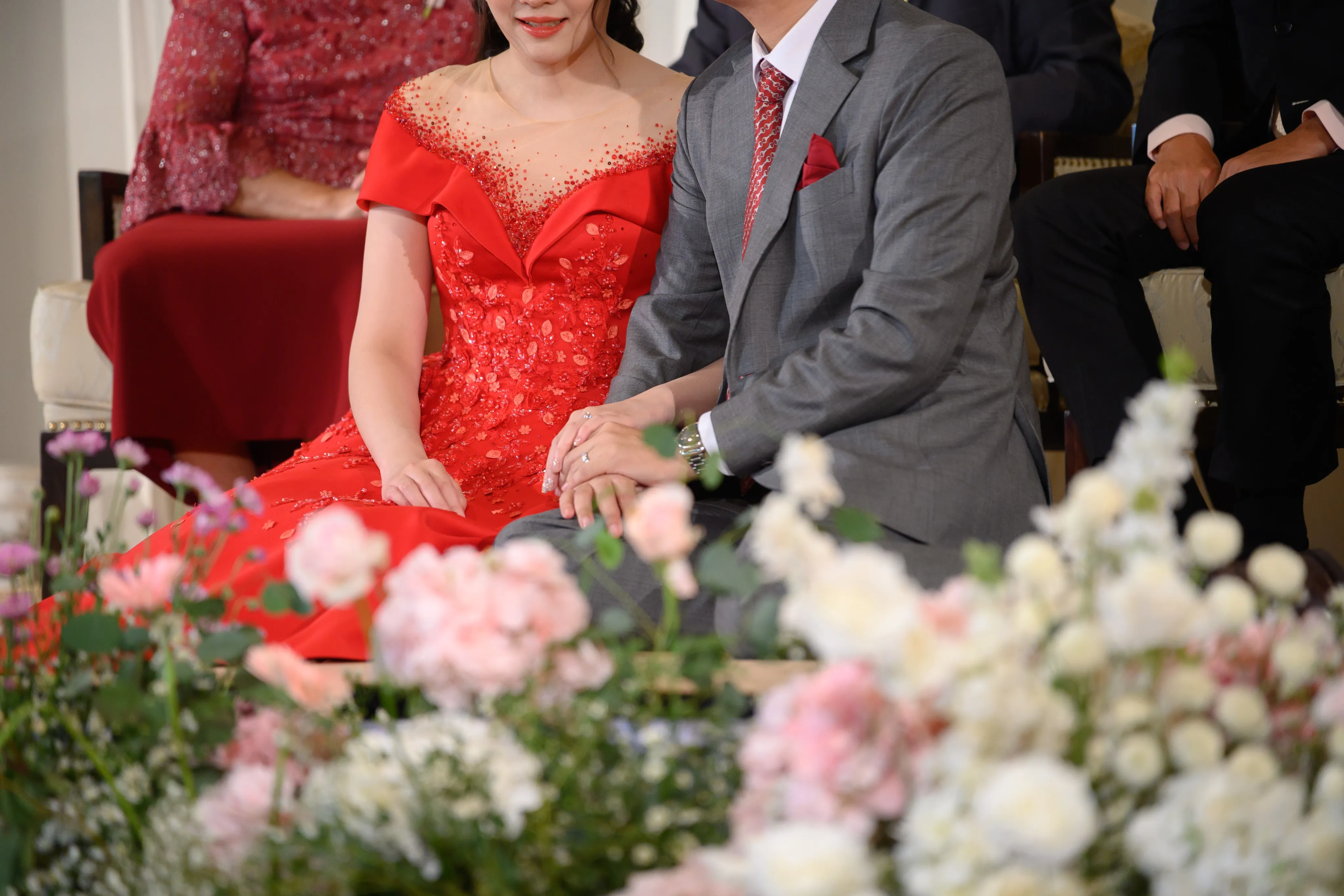 A couple in traditional red engagement attire holding hands during an engagement ceremony.