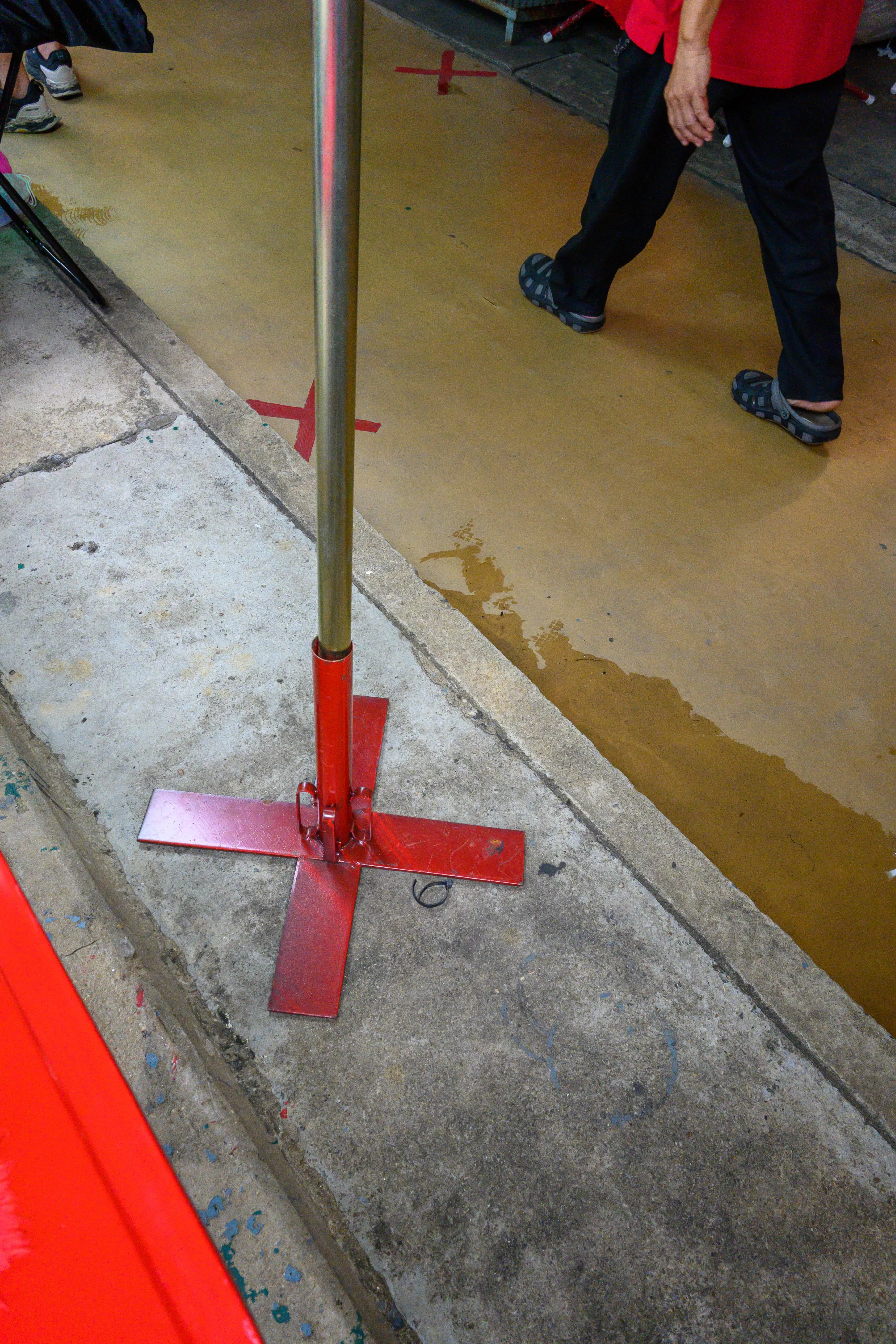 A red cross-shaped pole base on a freshly washed sidewalk as a pedestrian walks past
