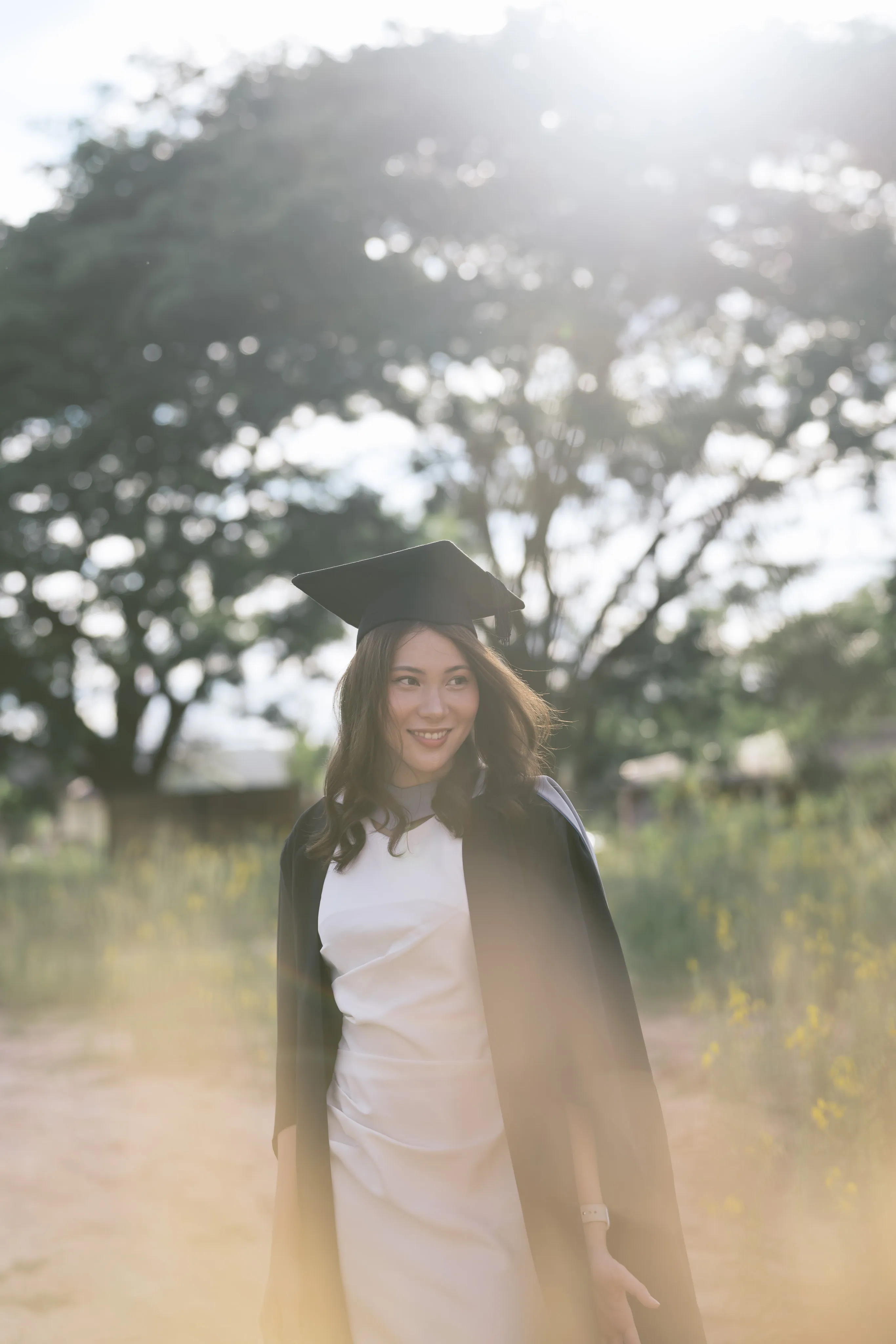 A graduate beneath trees in soft backlight