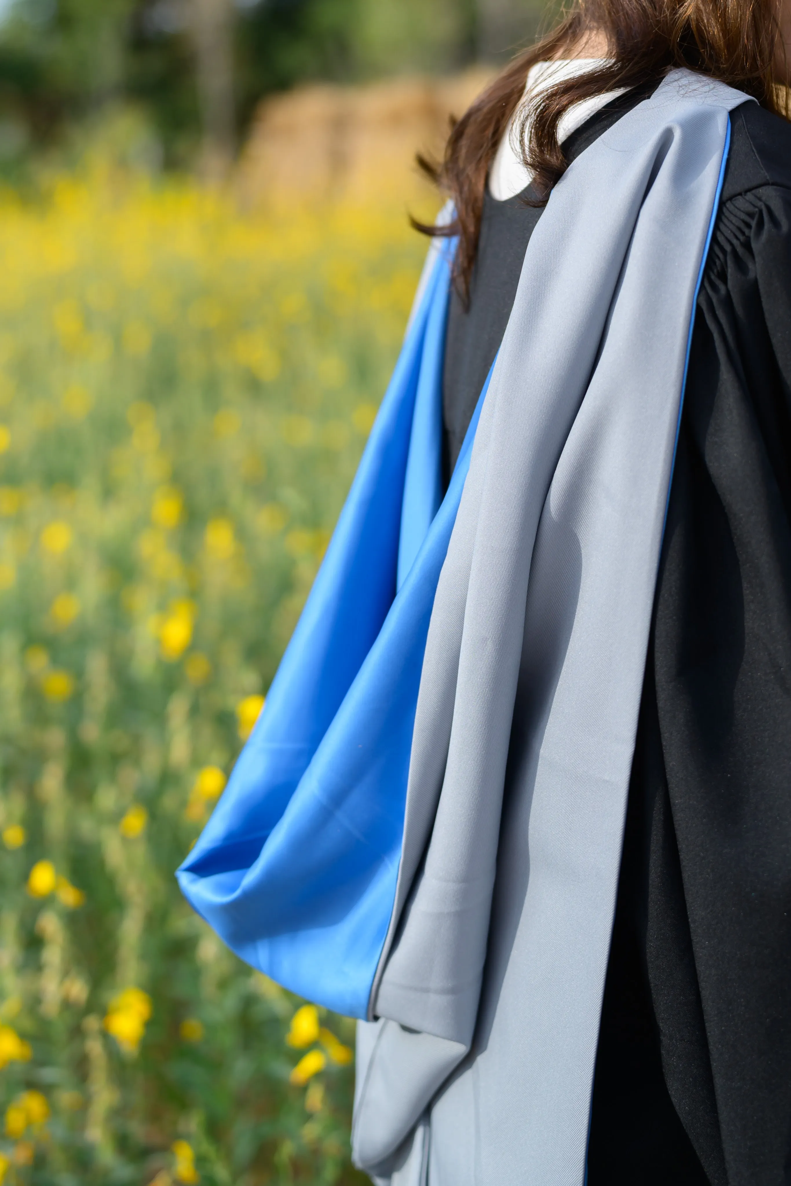 A close-up of a graduation gown and blue sash beside yellow flowers