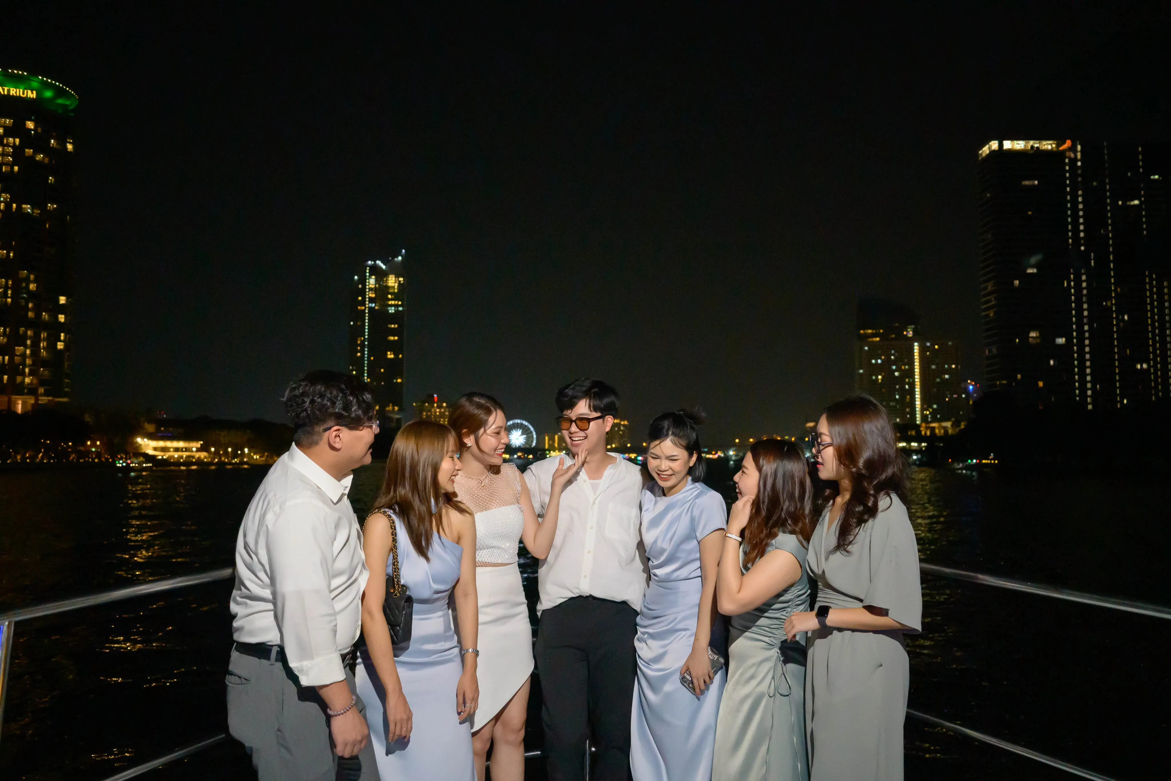 Friends gathered around a couple beside the water at night