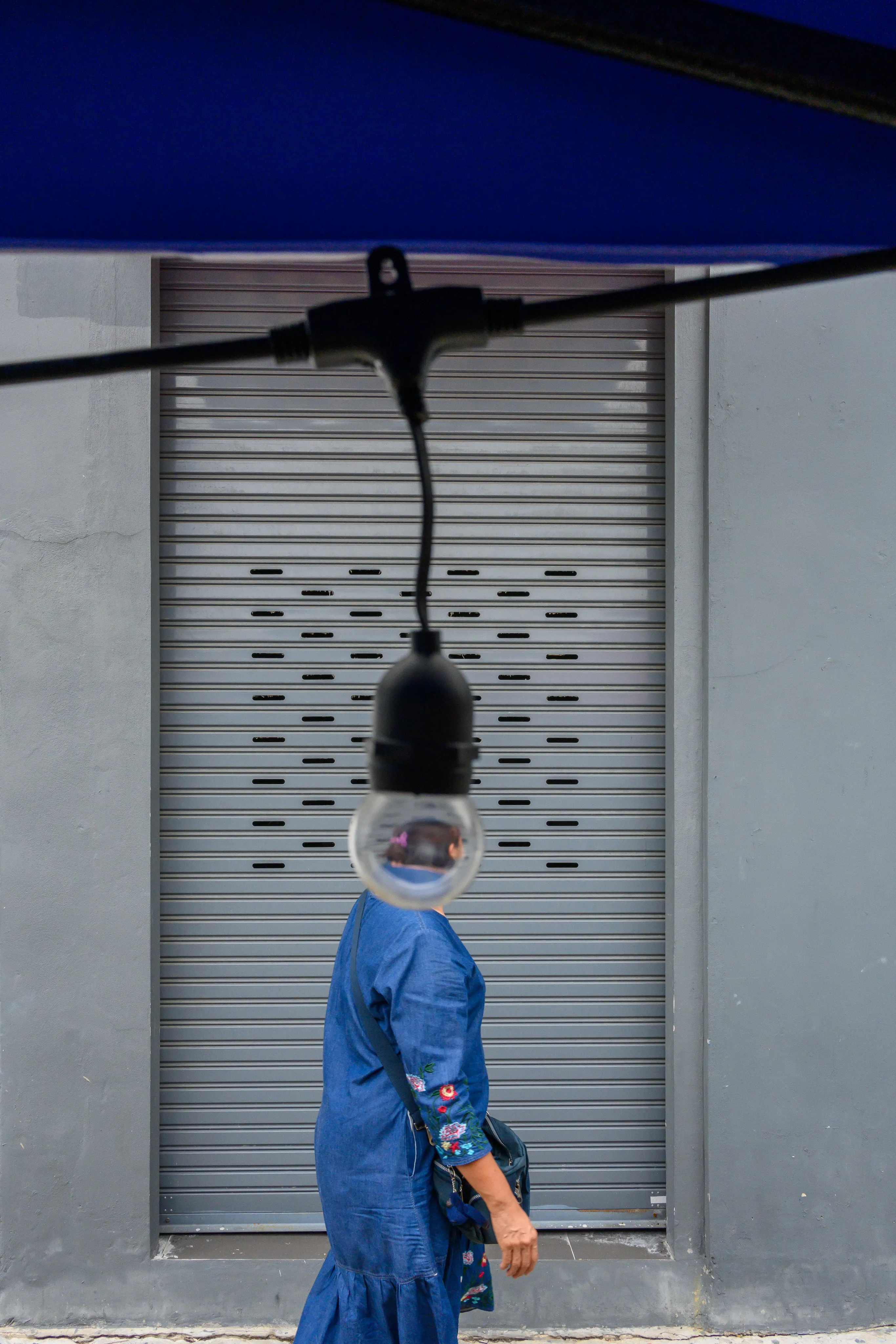 Woman walking beneath a hanging light bulb in front of a closed metal shutter