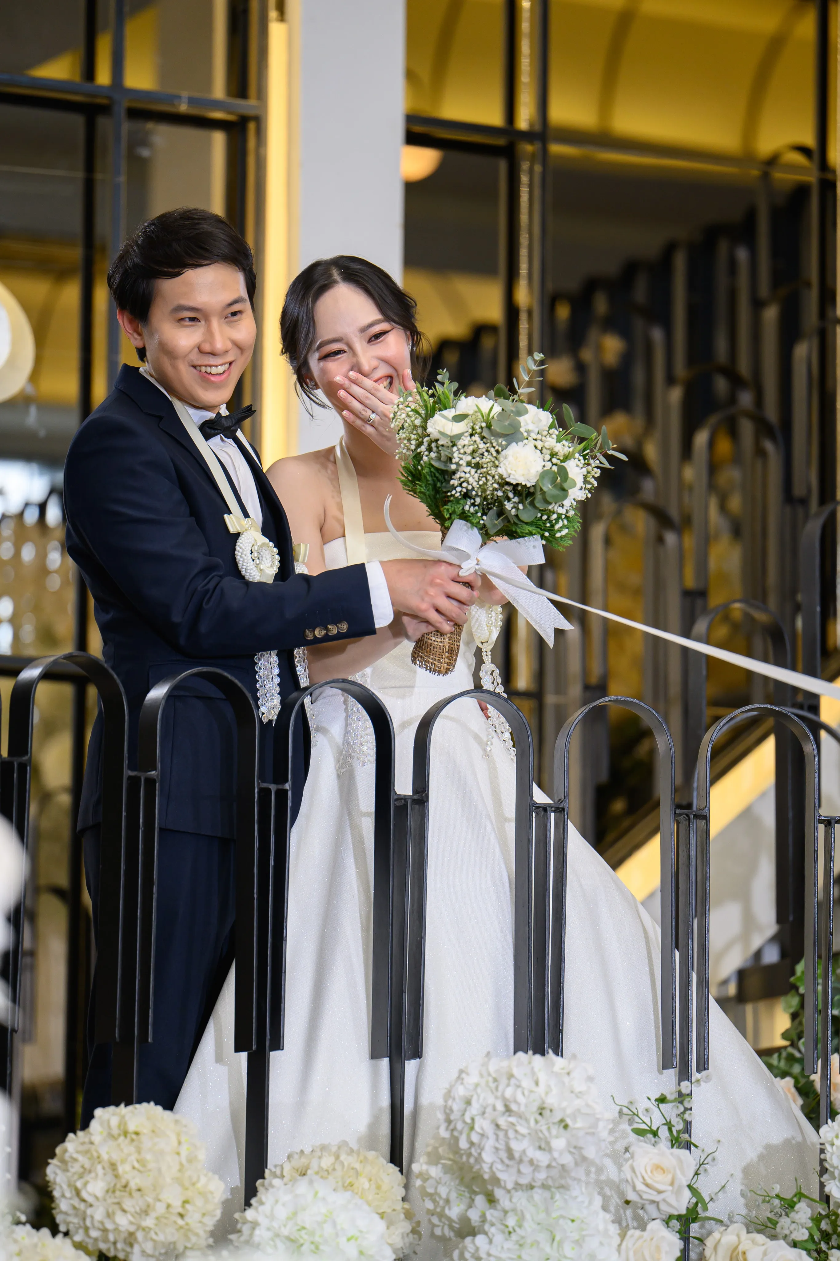 A bride and groom smiling together beside a staircase
