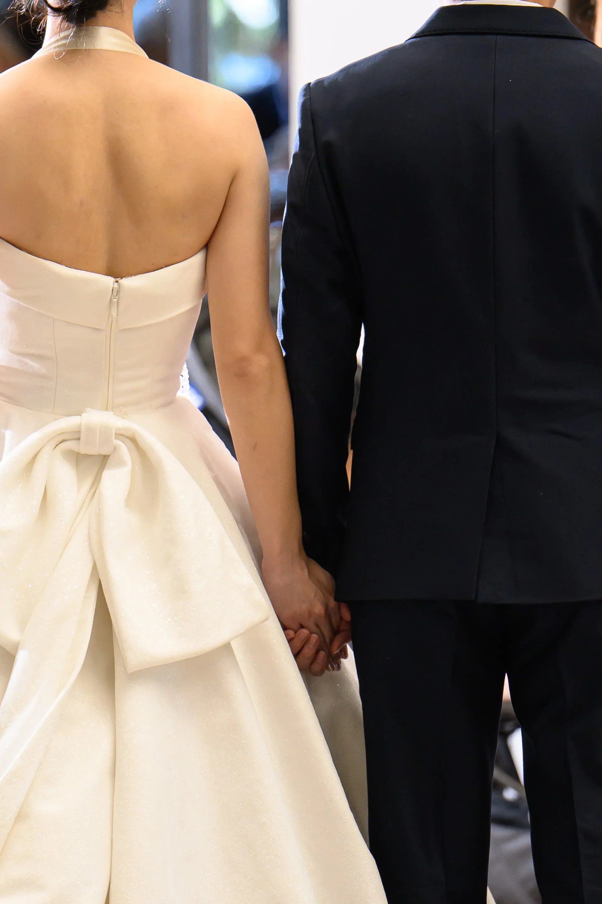 The back of a bridal gown beside the groom in a dark suit