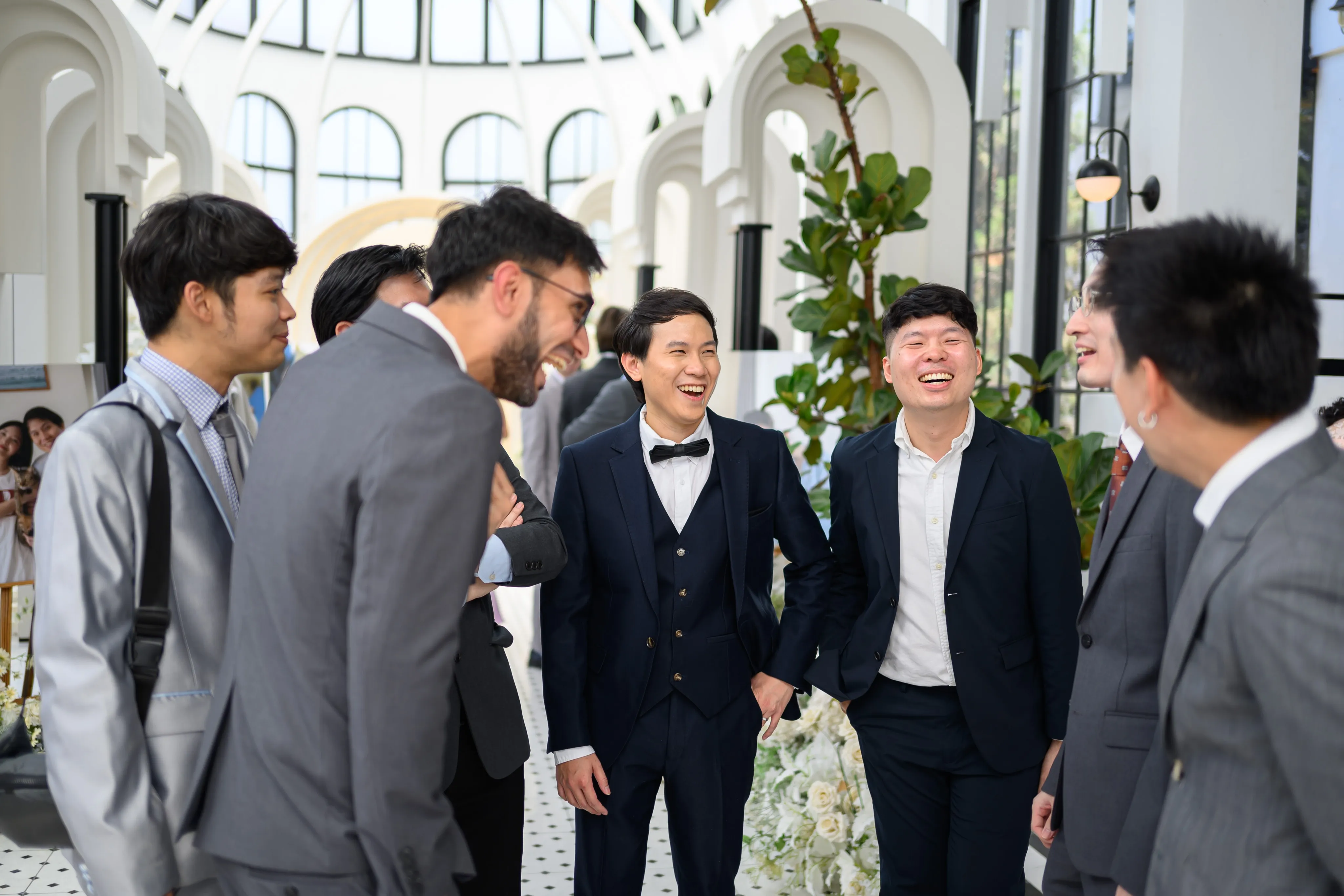 The groom laughing with friends in a bright reception hall