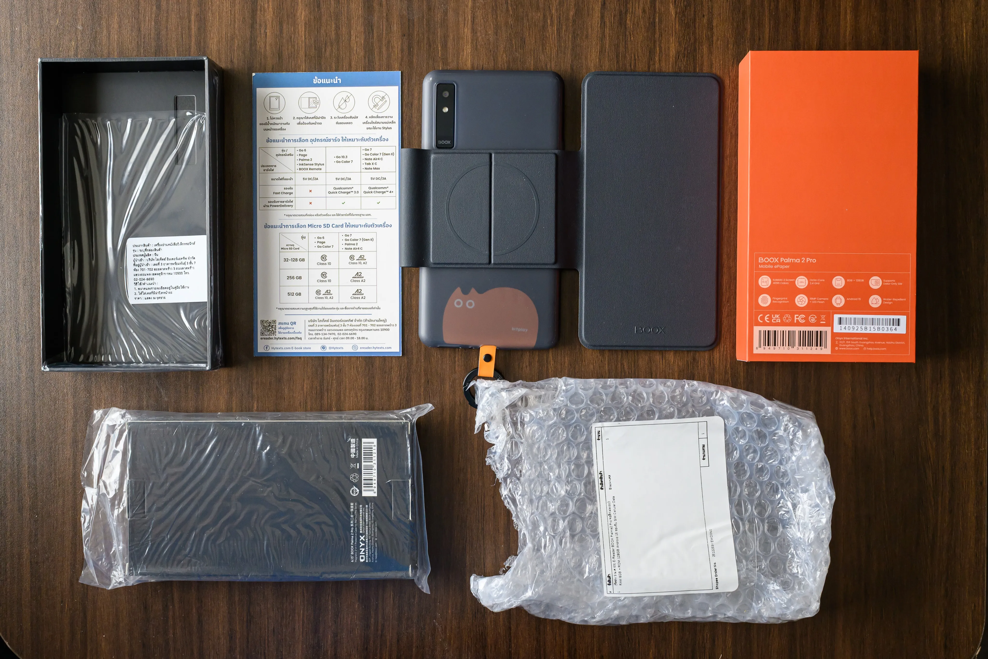 Flat lay of a phone, cases, manuals, and packaging arranged on a wood table
