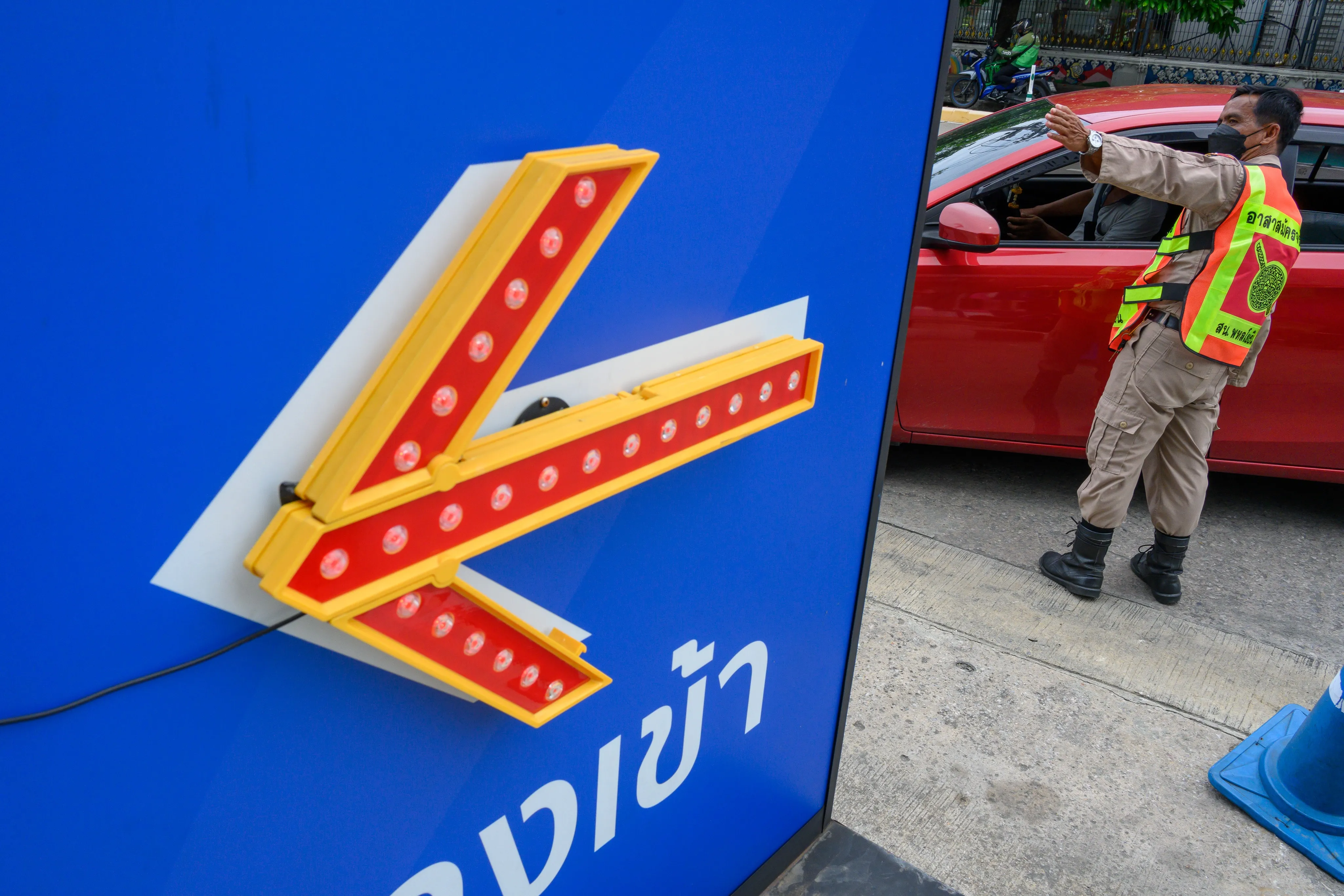 Illuminated red arrow sign pointing down toward Thai lettering on a blue wall