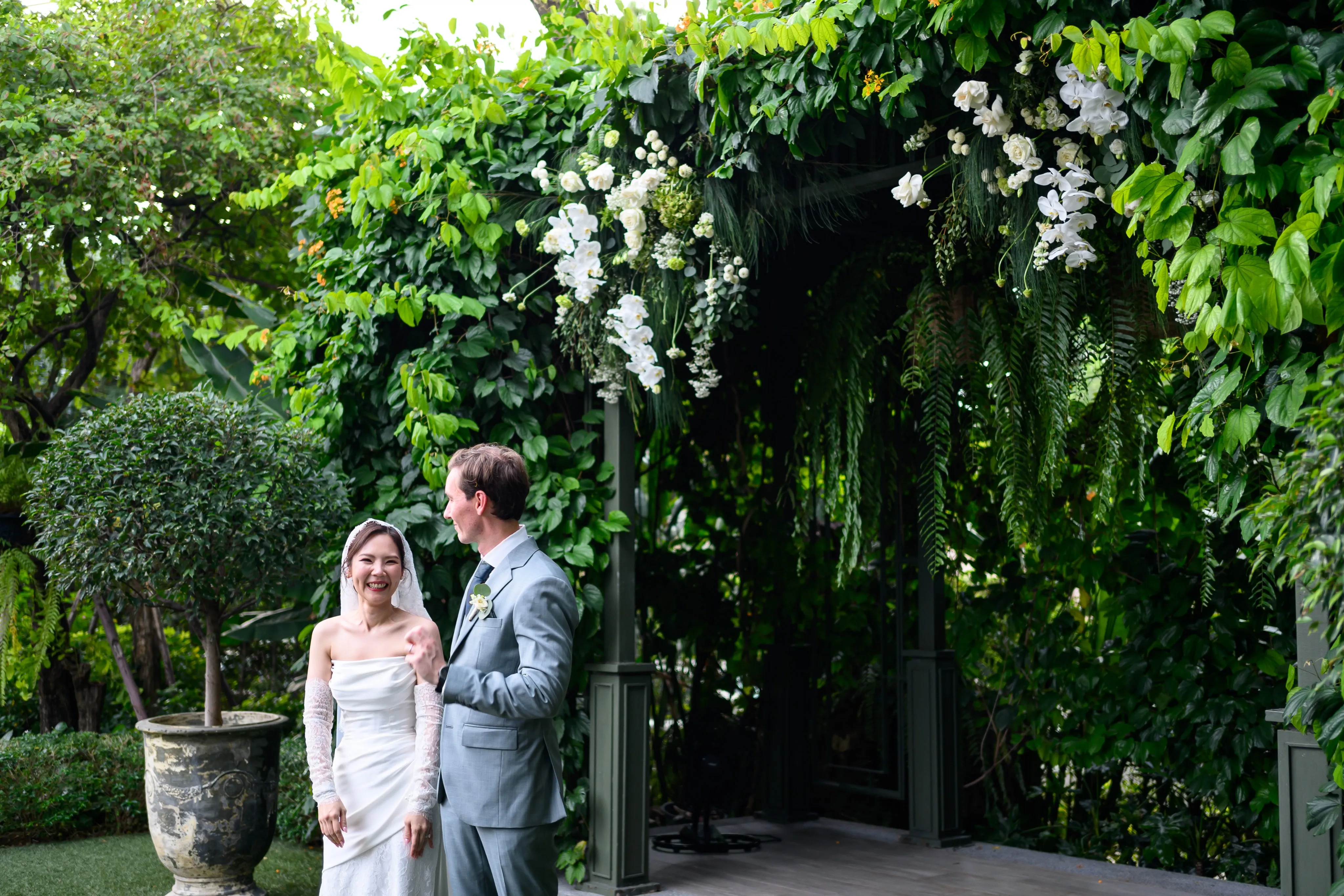 A wedding couple standing in a garden beneath hanging greenery