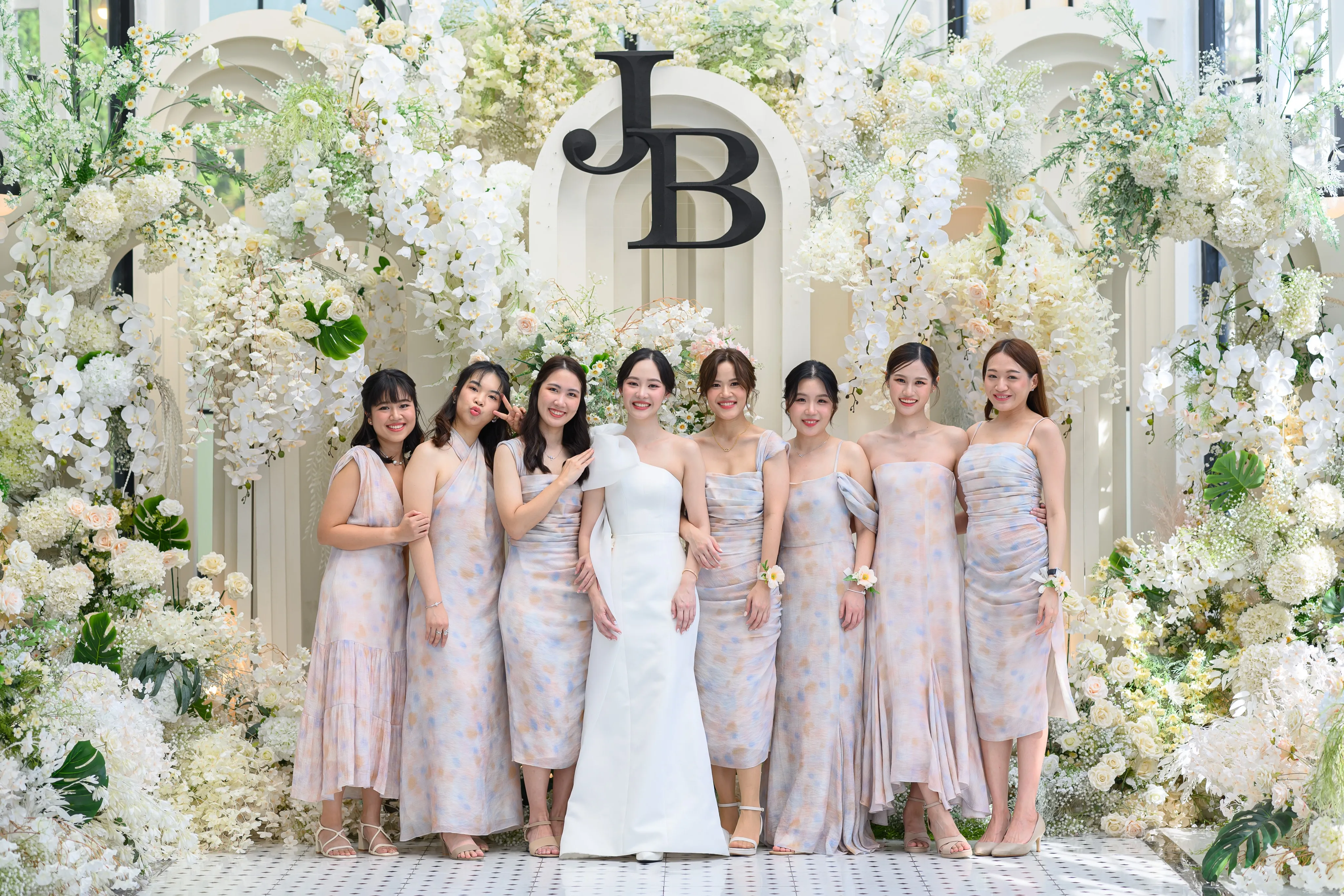 A group of bridesmaids beside a bride under white flowers