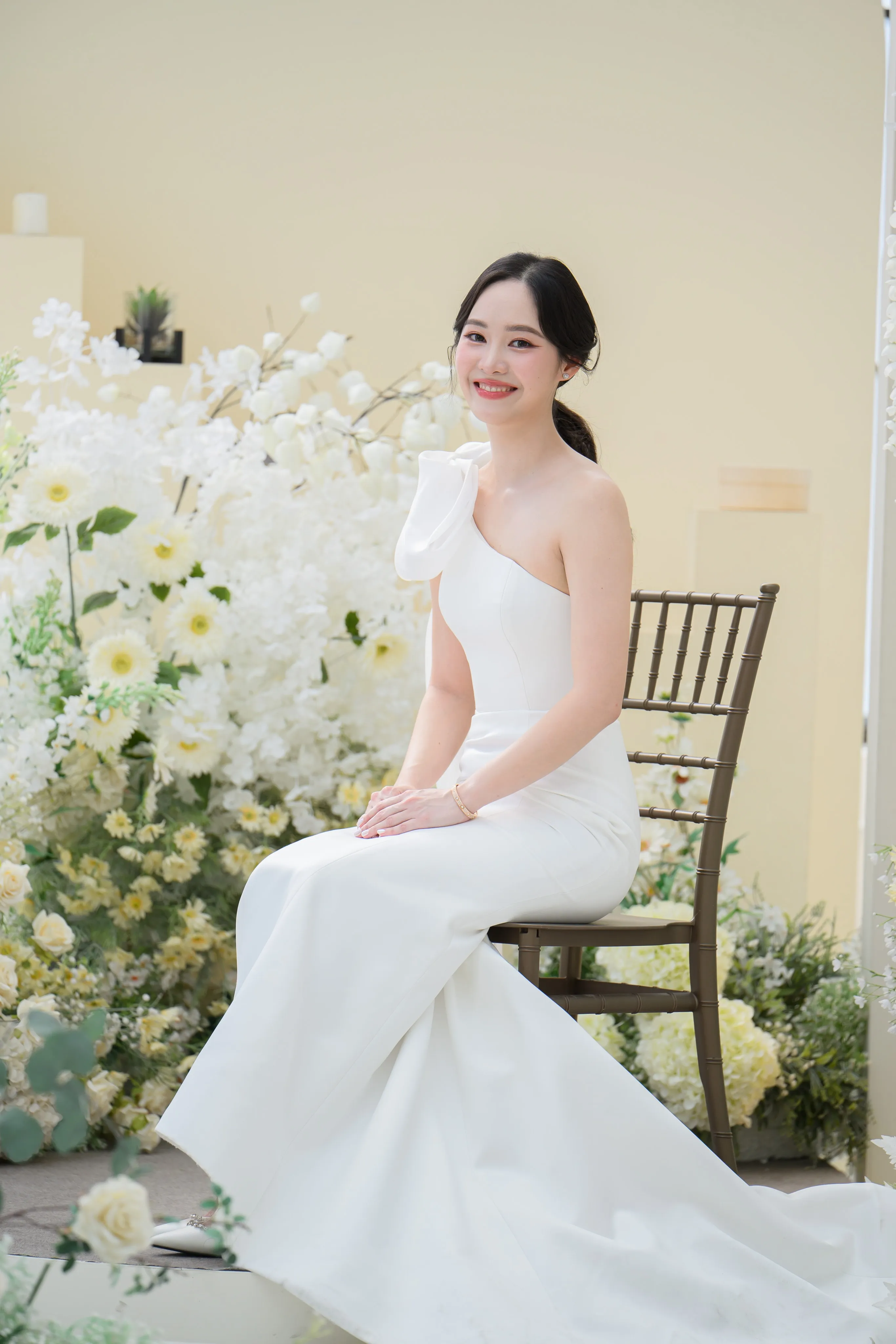 A bride seated in soft light beside a floral arrangement