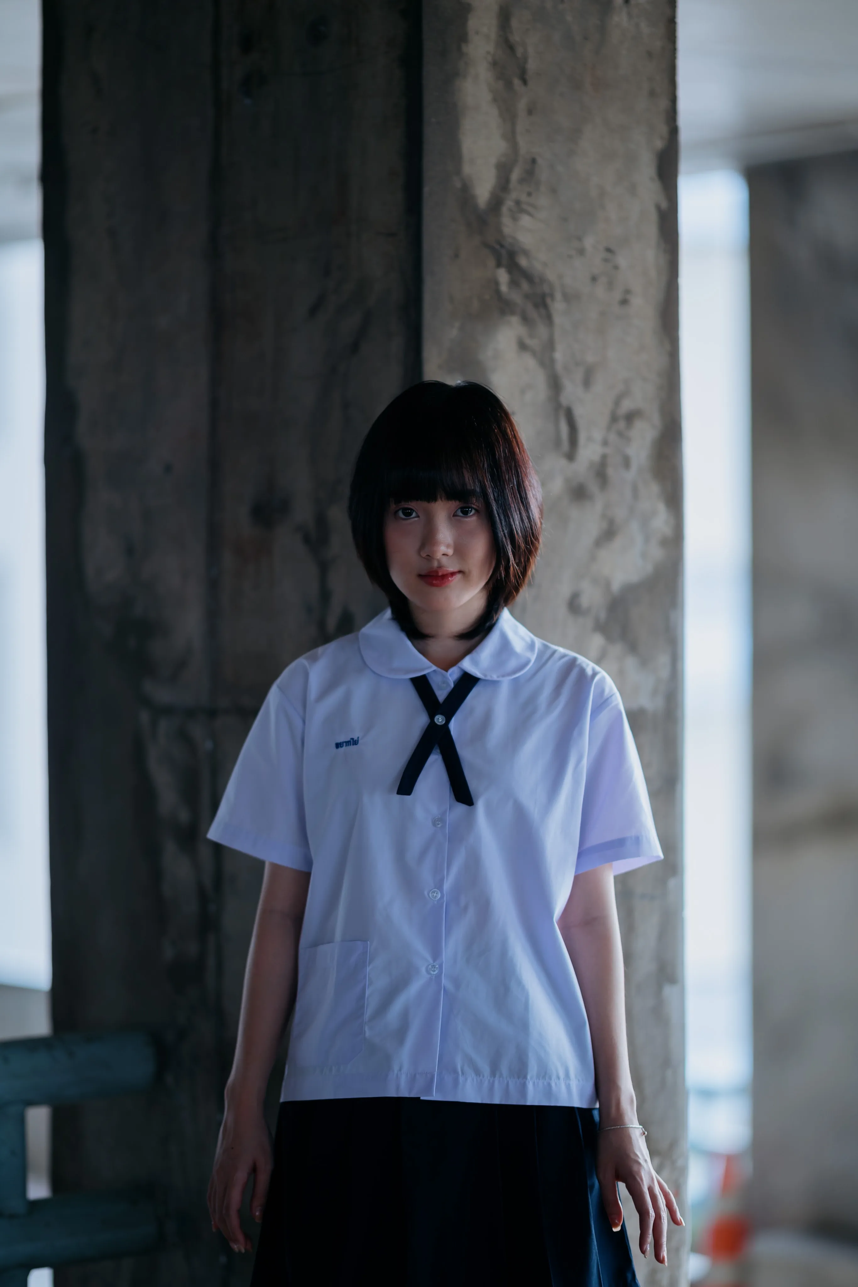A young woman in a school uniform standing in a concrete corridor