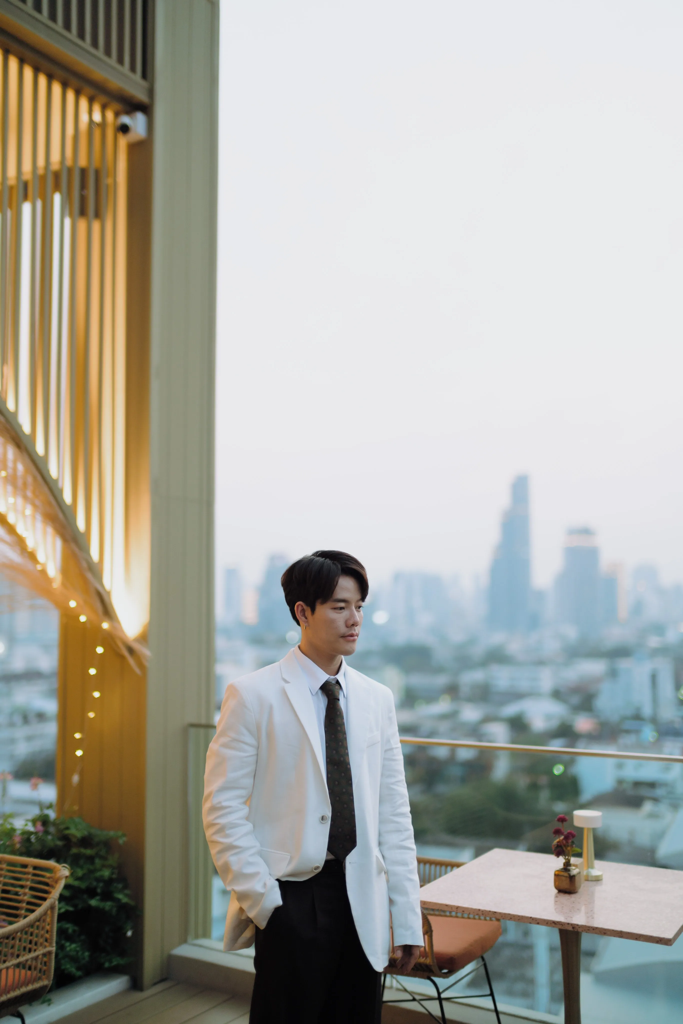 A man in a white shirt and dark tie beside a window overlooking the city