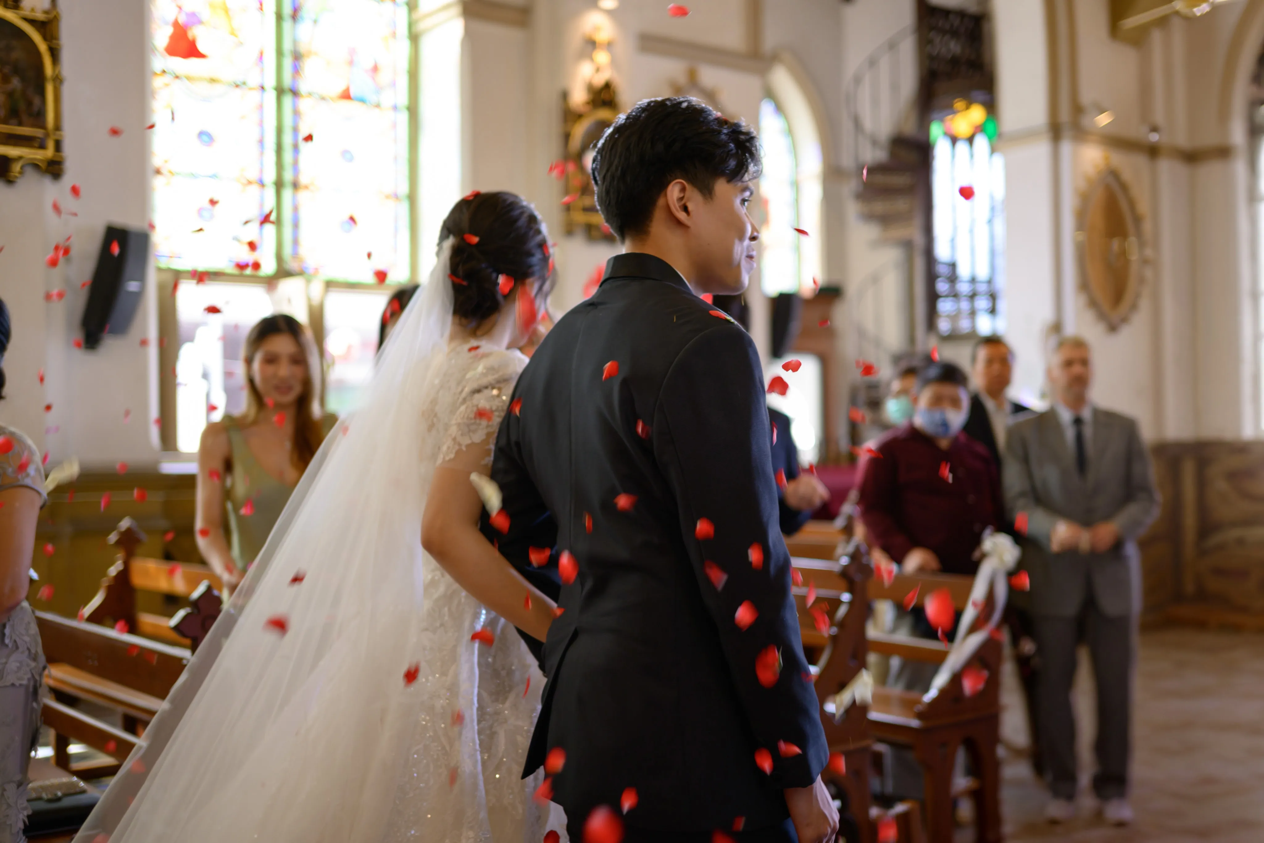 A bride and groom walking through a church aisle as red rose petals fall around them