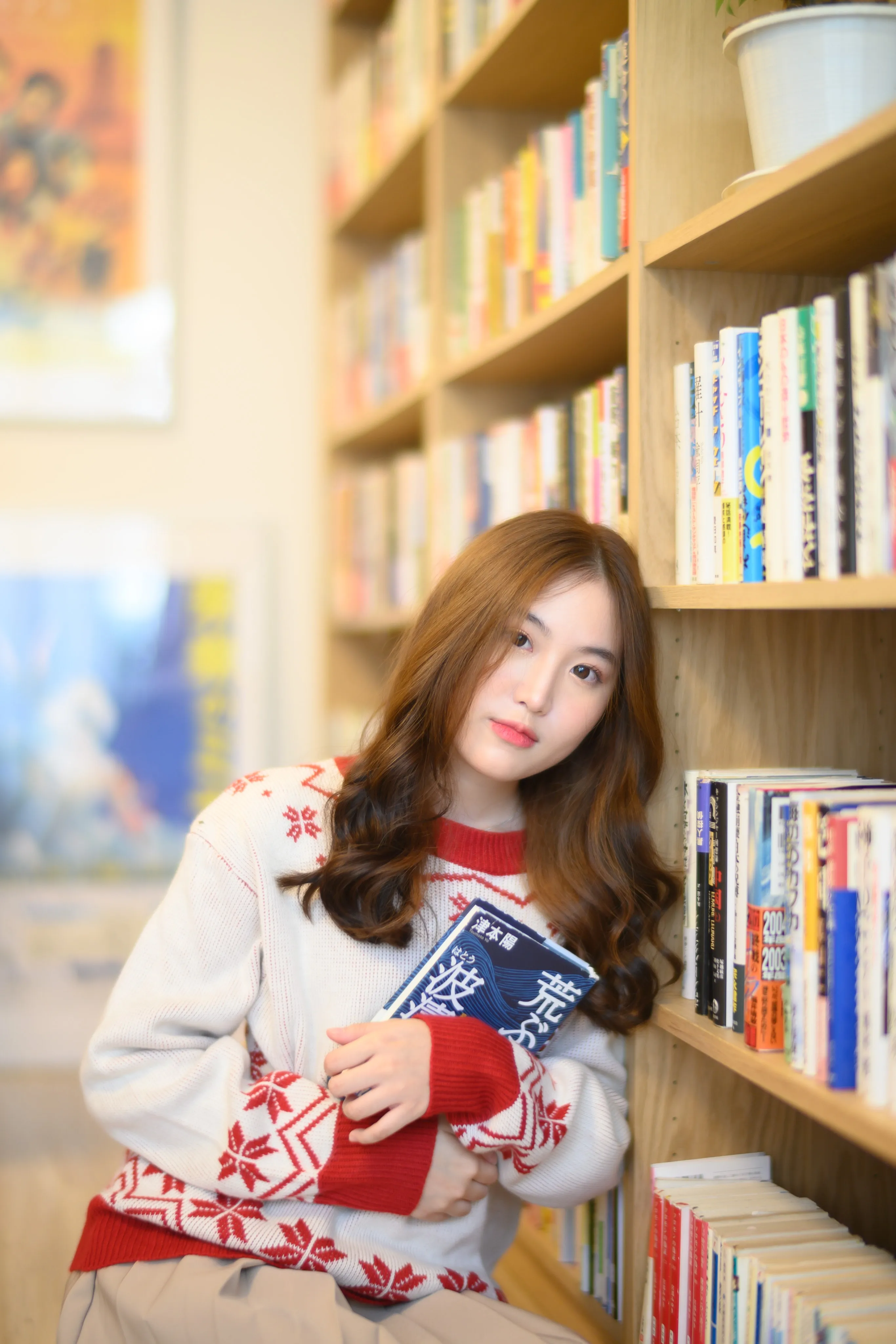Woman in a patterned sweater holding a blue book between tall library shelves