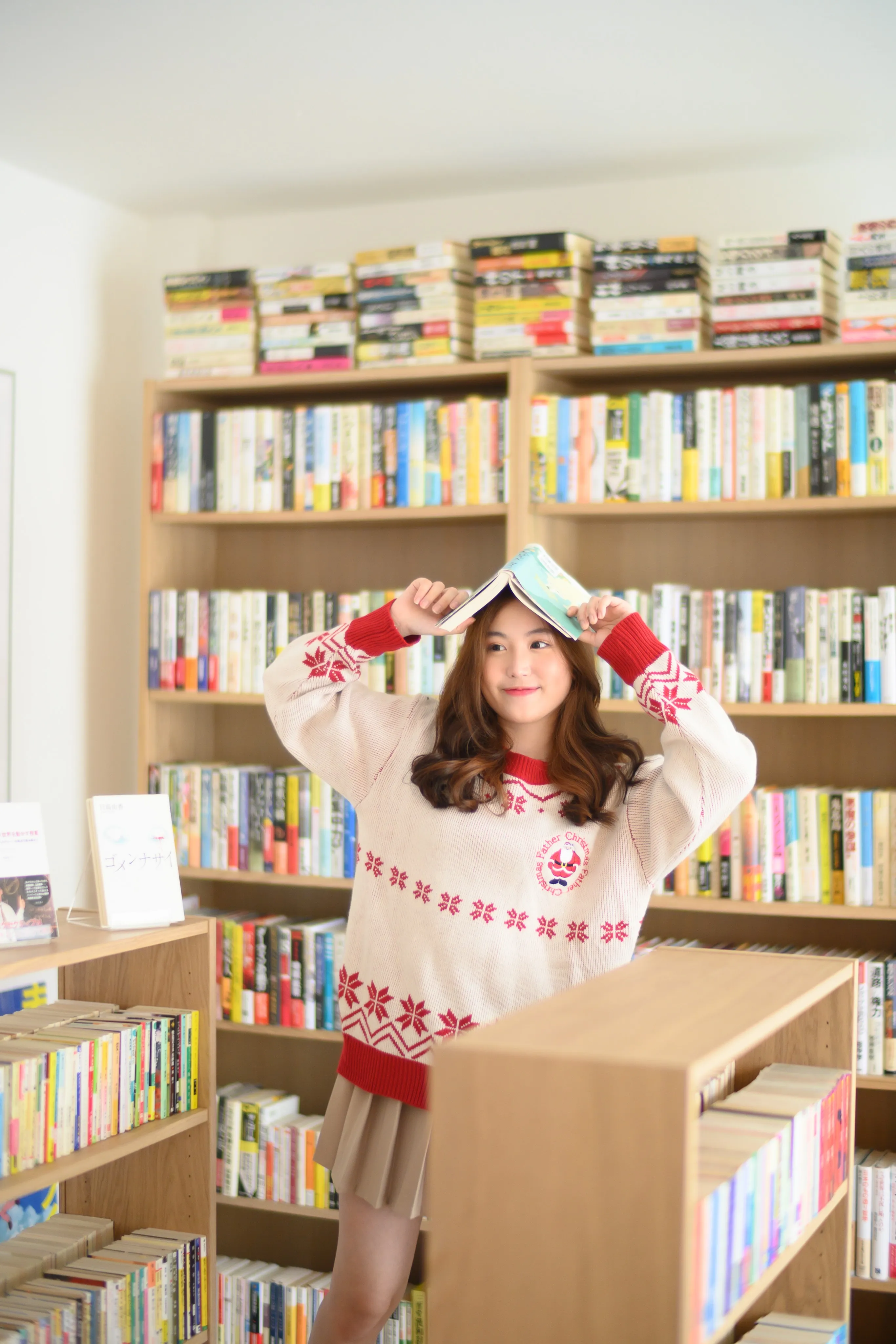 Woman playfully balancing open books above her head in a library aisle