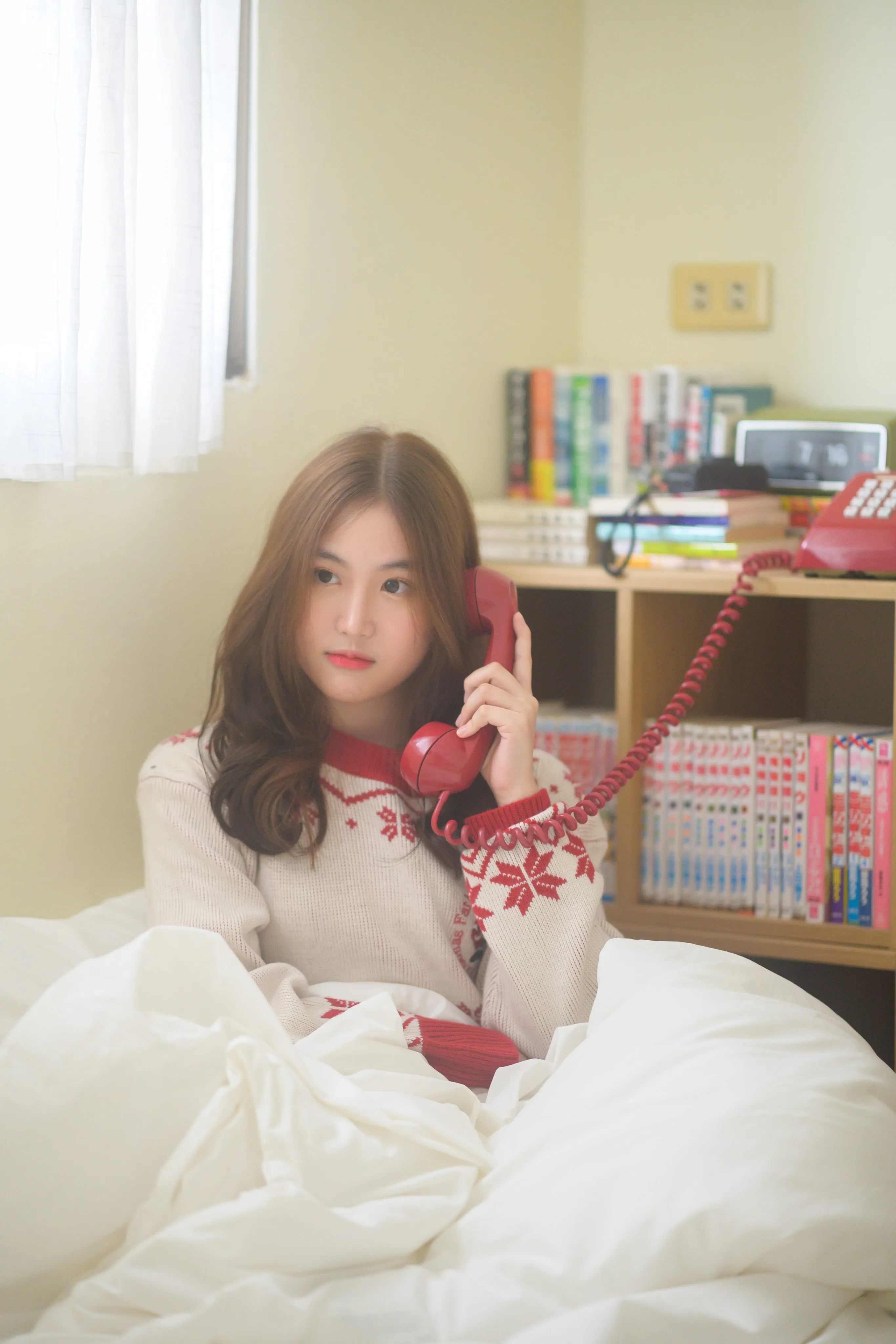 Woman sitting under a white duvet and holding a red telephone receiver