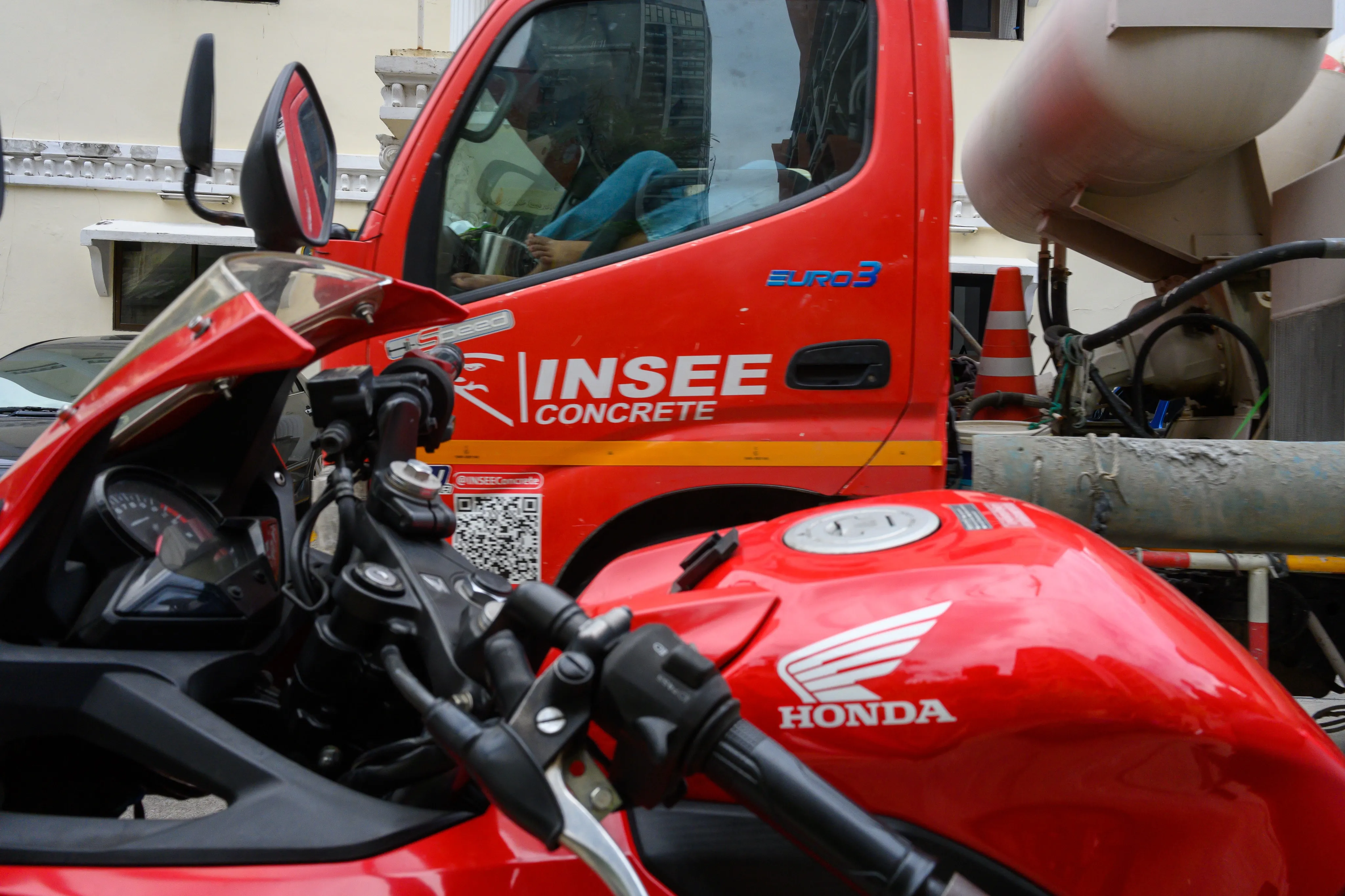 Red motorcycle parked between a concrete truck and construction equipment