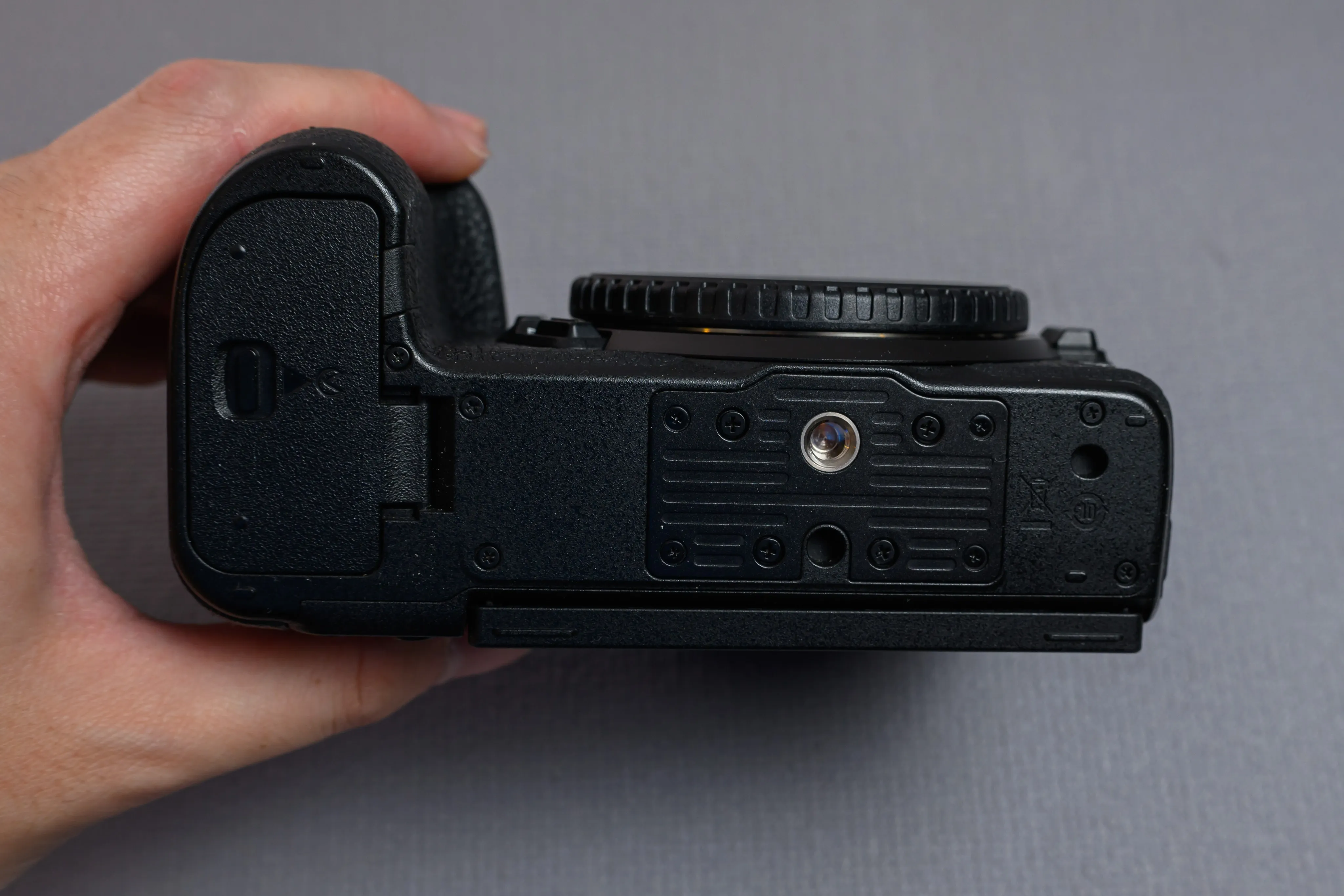 Hand holding the underside of a compact camera against a gray background