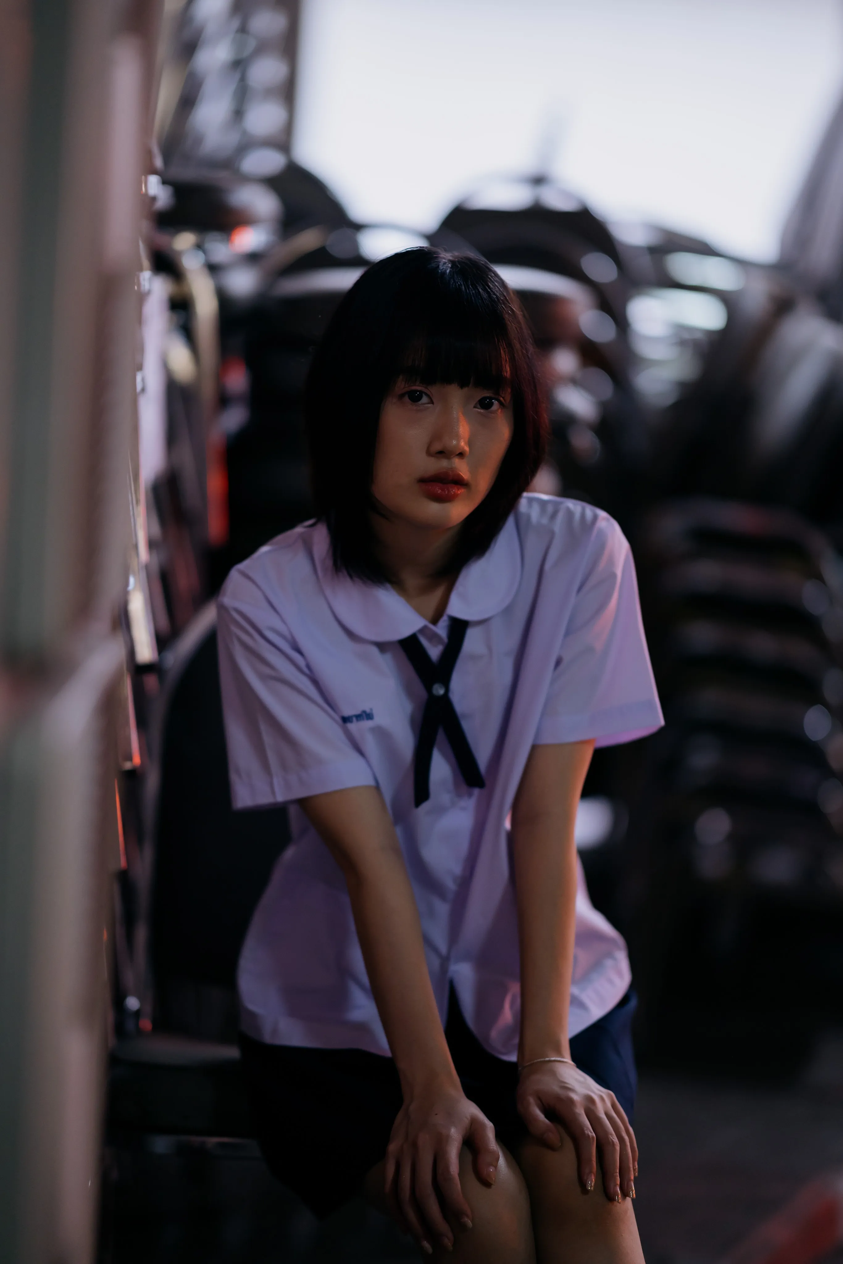 A young woman in a school uniform leaning forward in dramatic light