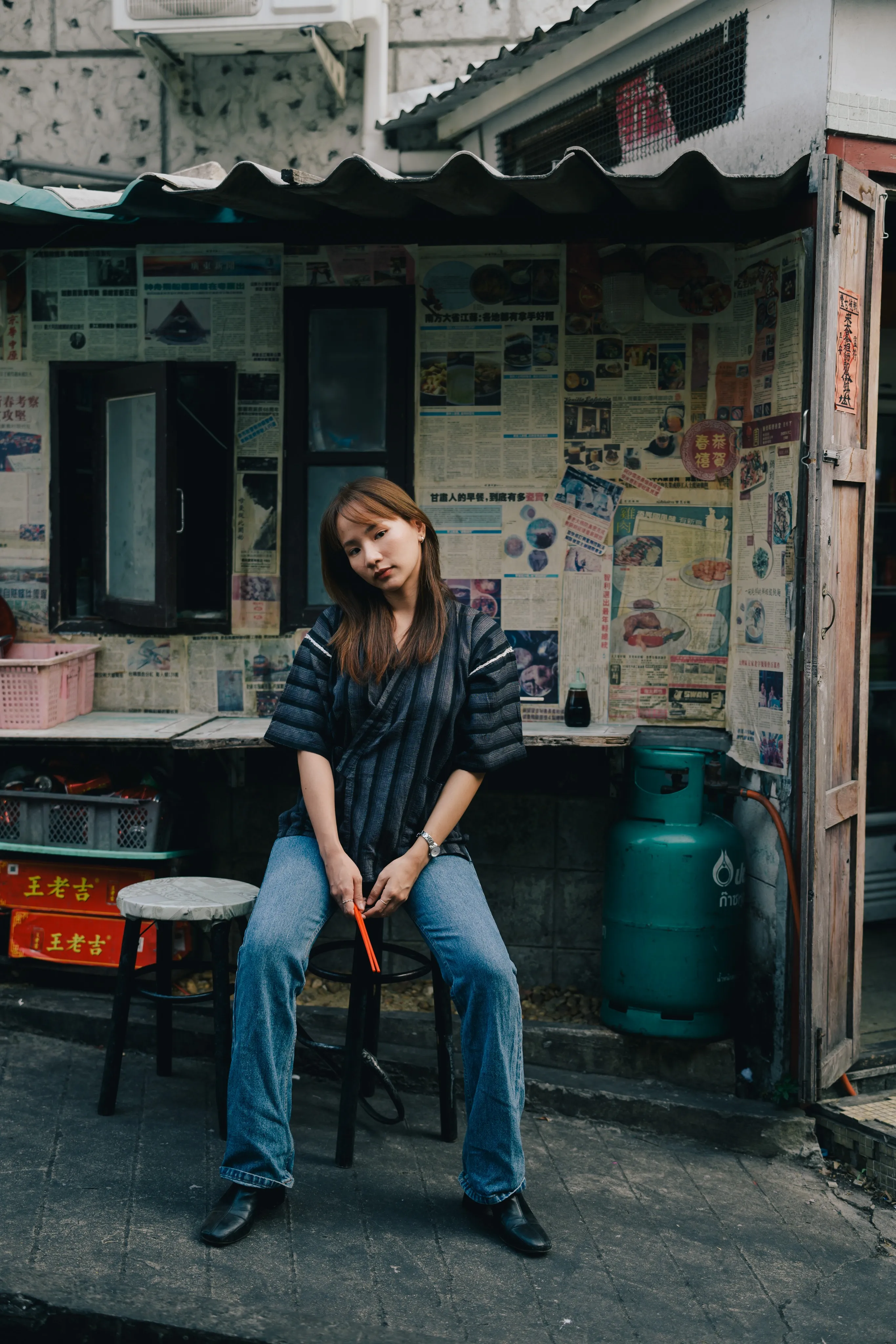 Woman seated outside a weathered storefront covered with posters and newspaper clippings
