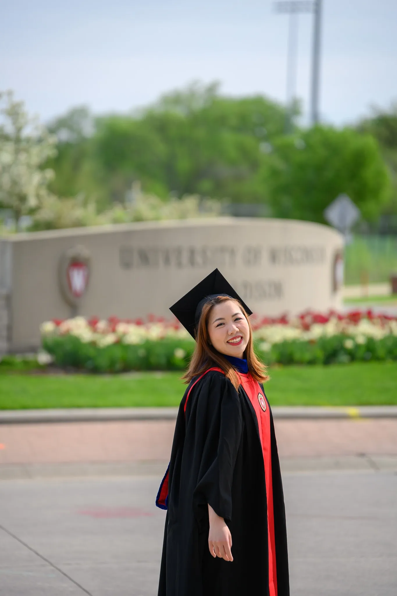 Graduate in cap and gown posing on campus in front of the University of Wisconsin–Madison sign