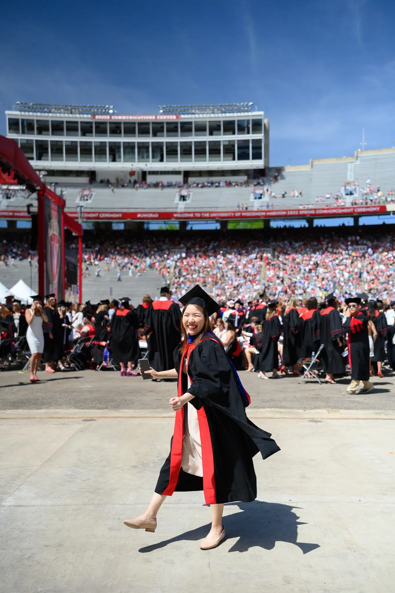 Graduate walking across a stadium field during a sunny commencement ceremony