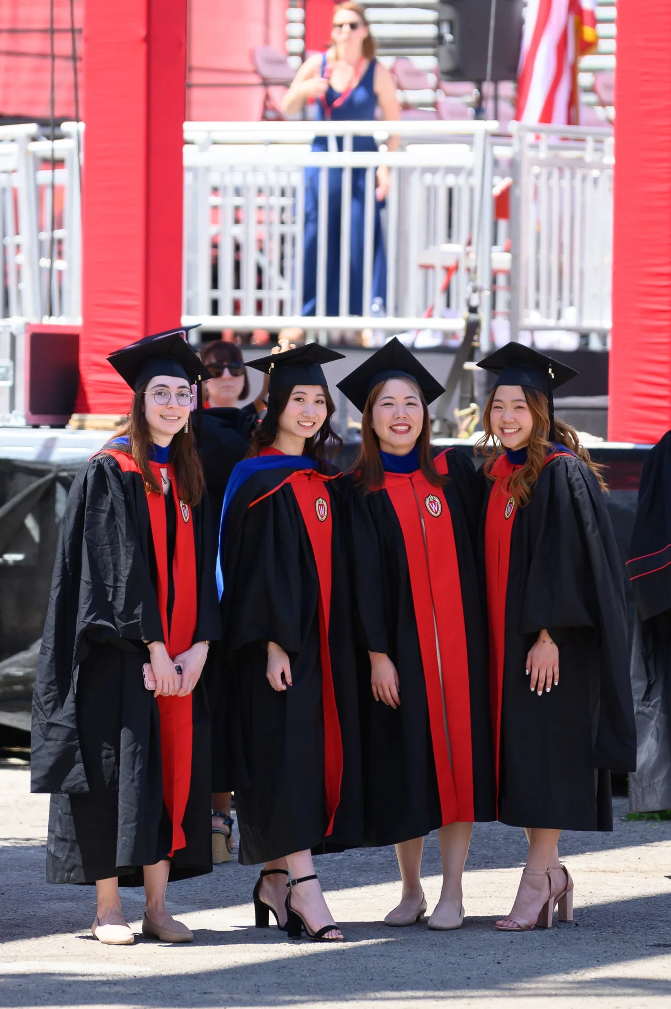 Four graduates in black and red regalia posing together outdoors