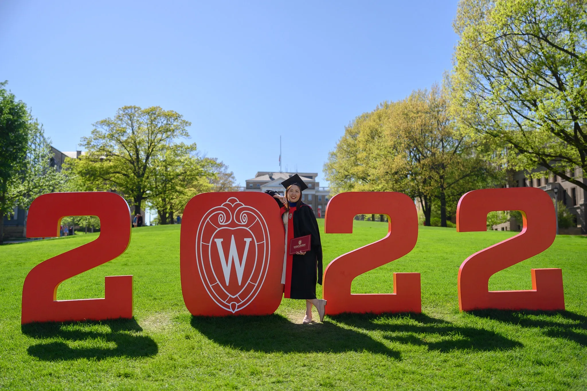 Graduate standing between large red 2s and a Wisconsin emblem on a lawn
