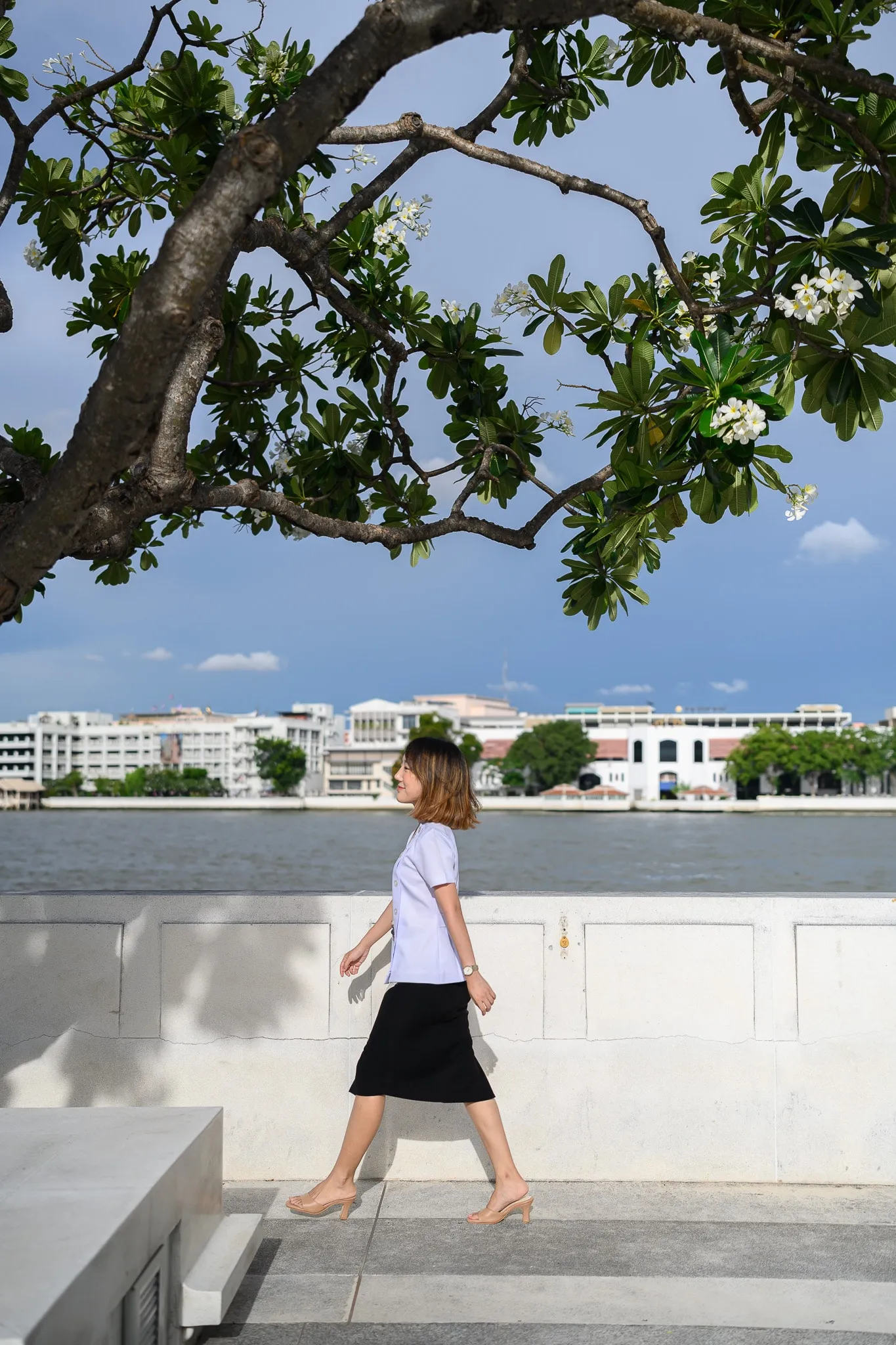 Woman walking beside a river beneath a leafy tree