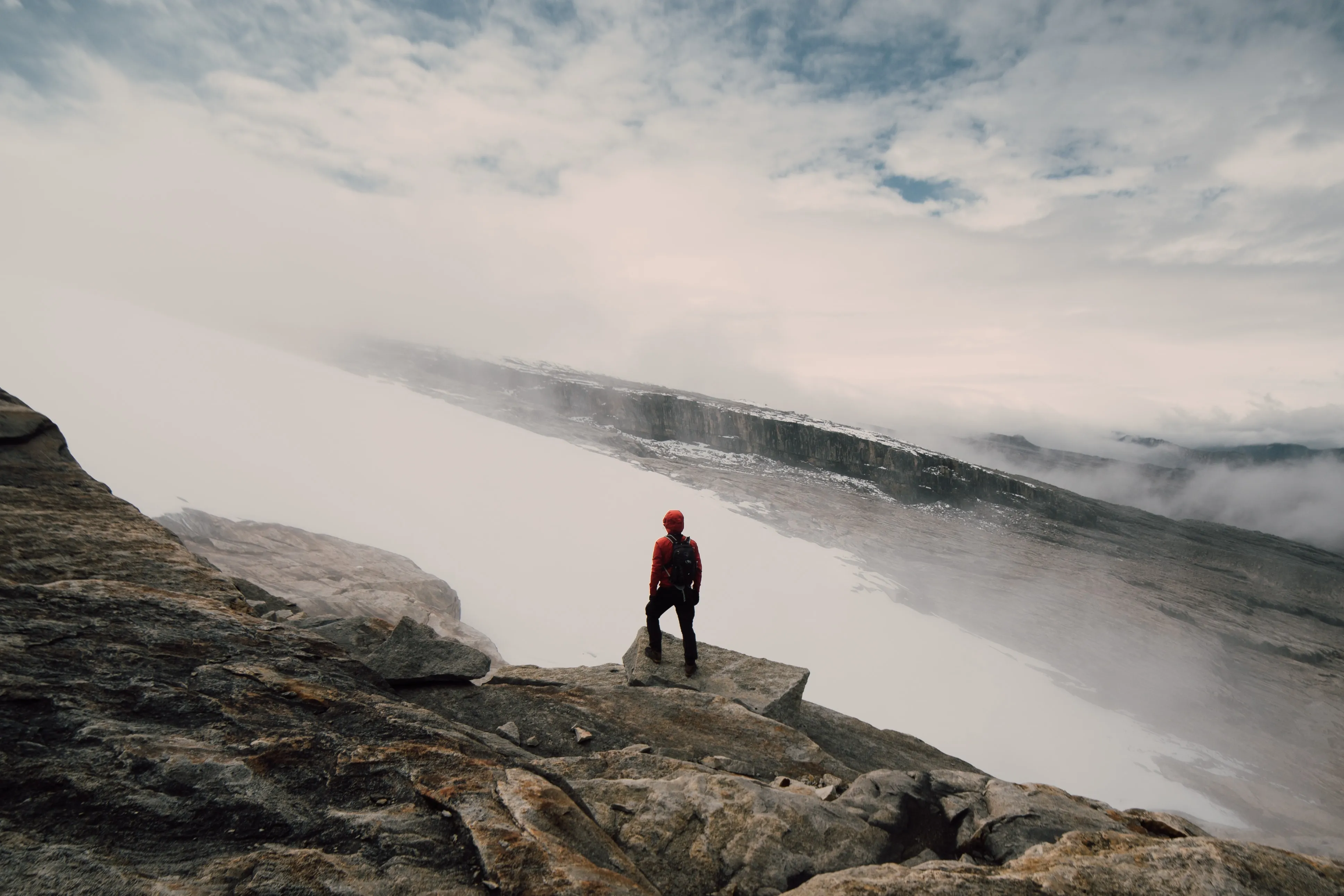 A lone figure standing on a cliff above a sea of clouds
