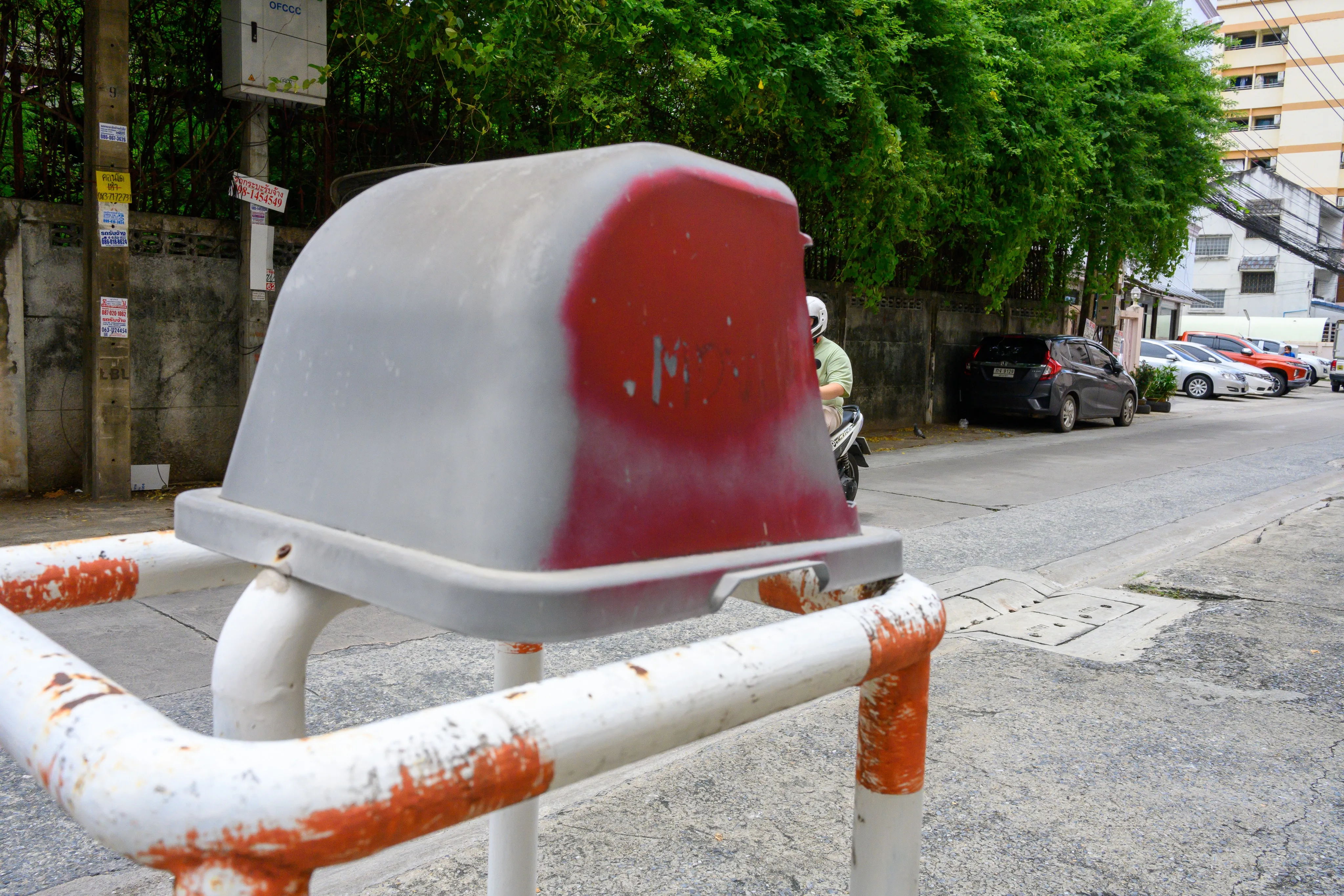 Faded red-and-white concrete bollard beneath a leafy tree on a quiet street