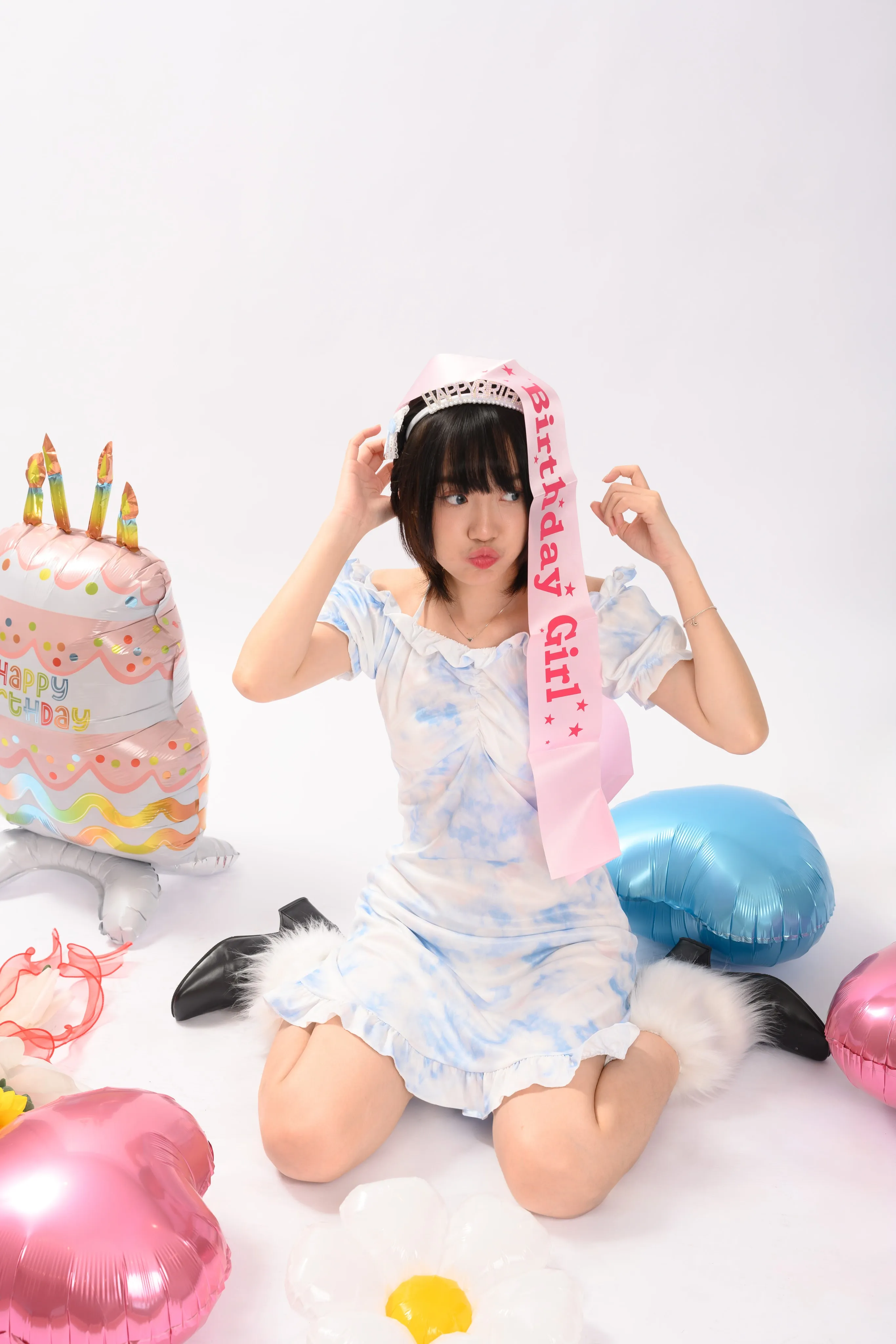 A woman wearing a 'birthday girl' sash surrounded by balloons