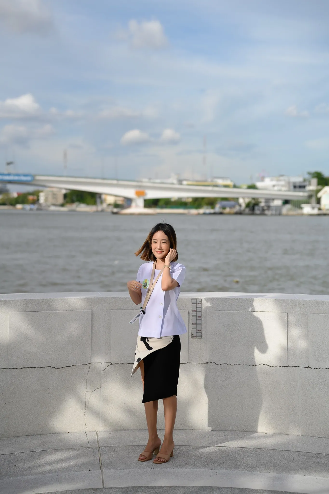 Woman standing by a riverside wall with a bridge and skyline behind her