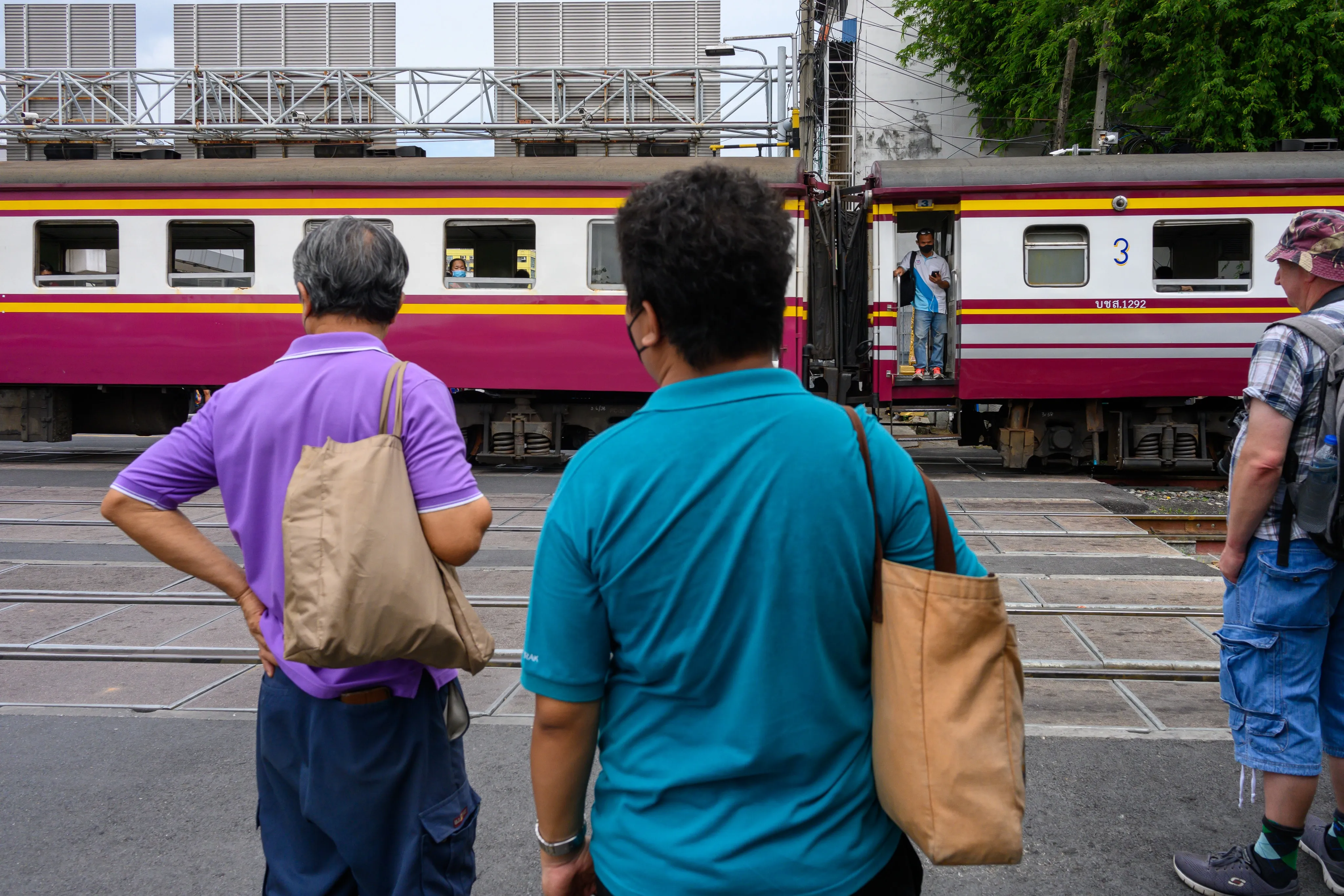 Two men watching a cream-and-red passenger train at a station platform