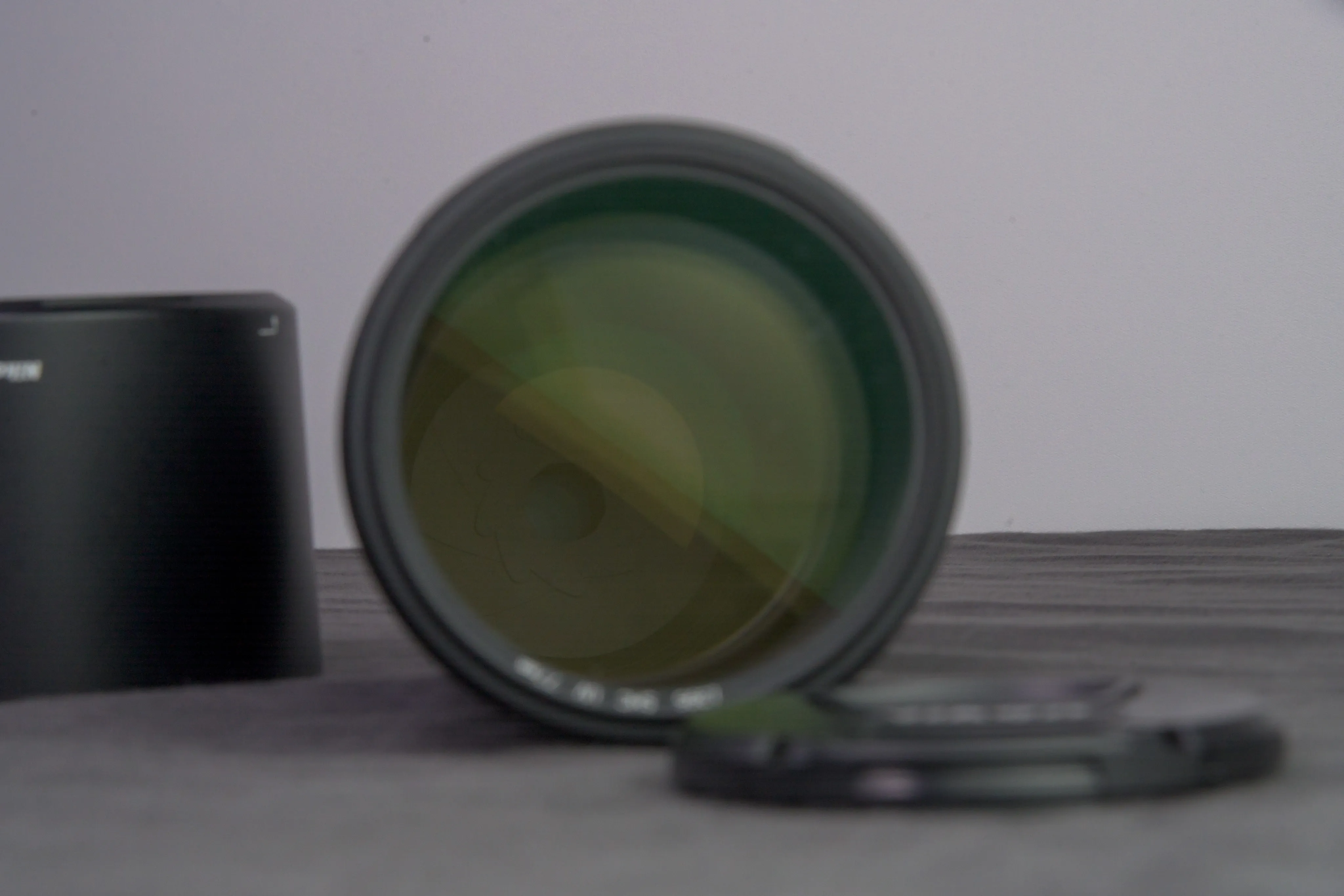 A large camera lens beside its hood and front cap on a gray surface