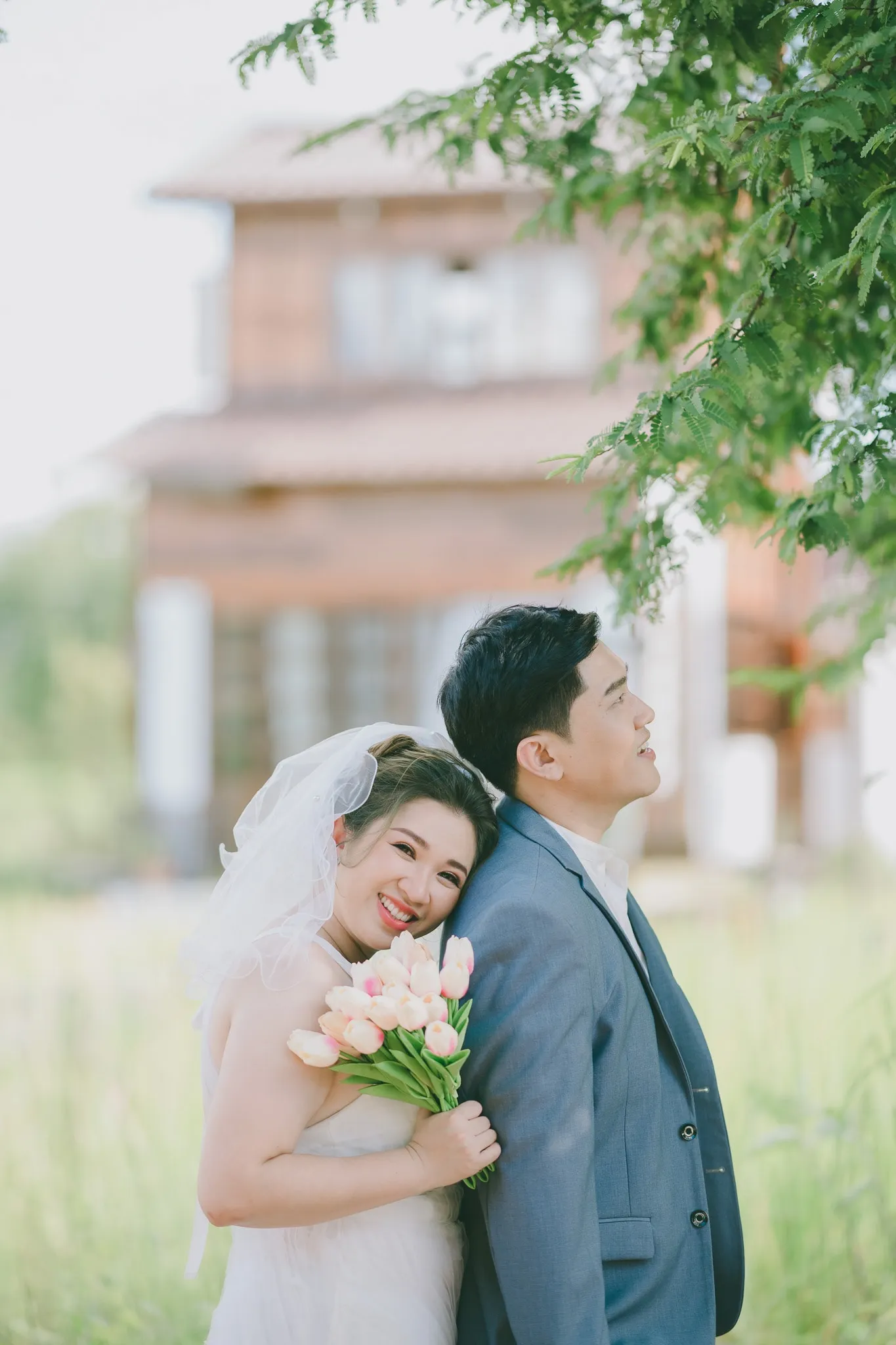 A smiling bride with a tulip bouquet leaning back to back with her partner in a grey suit